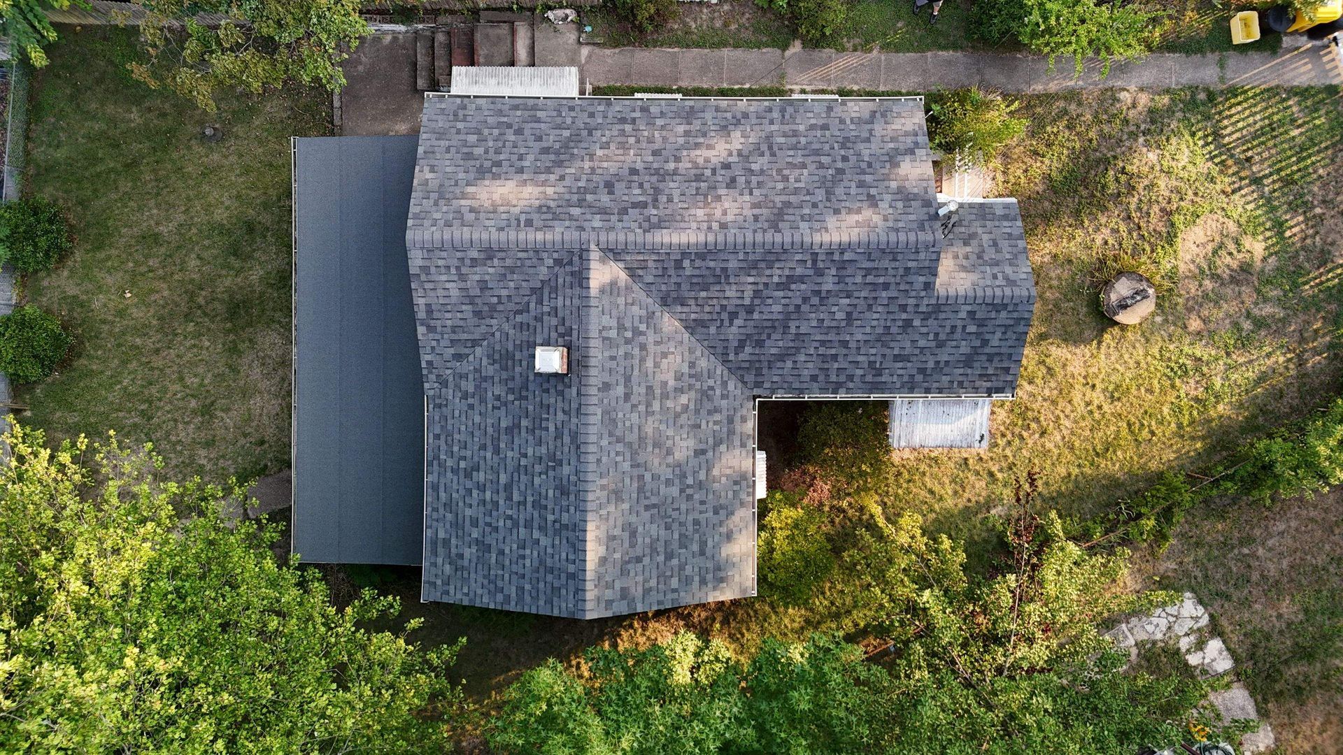An aerial view of a house with a roof surrounded by trees and grass.