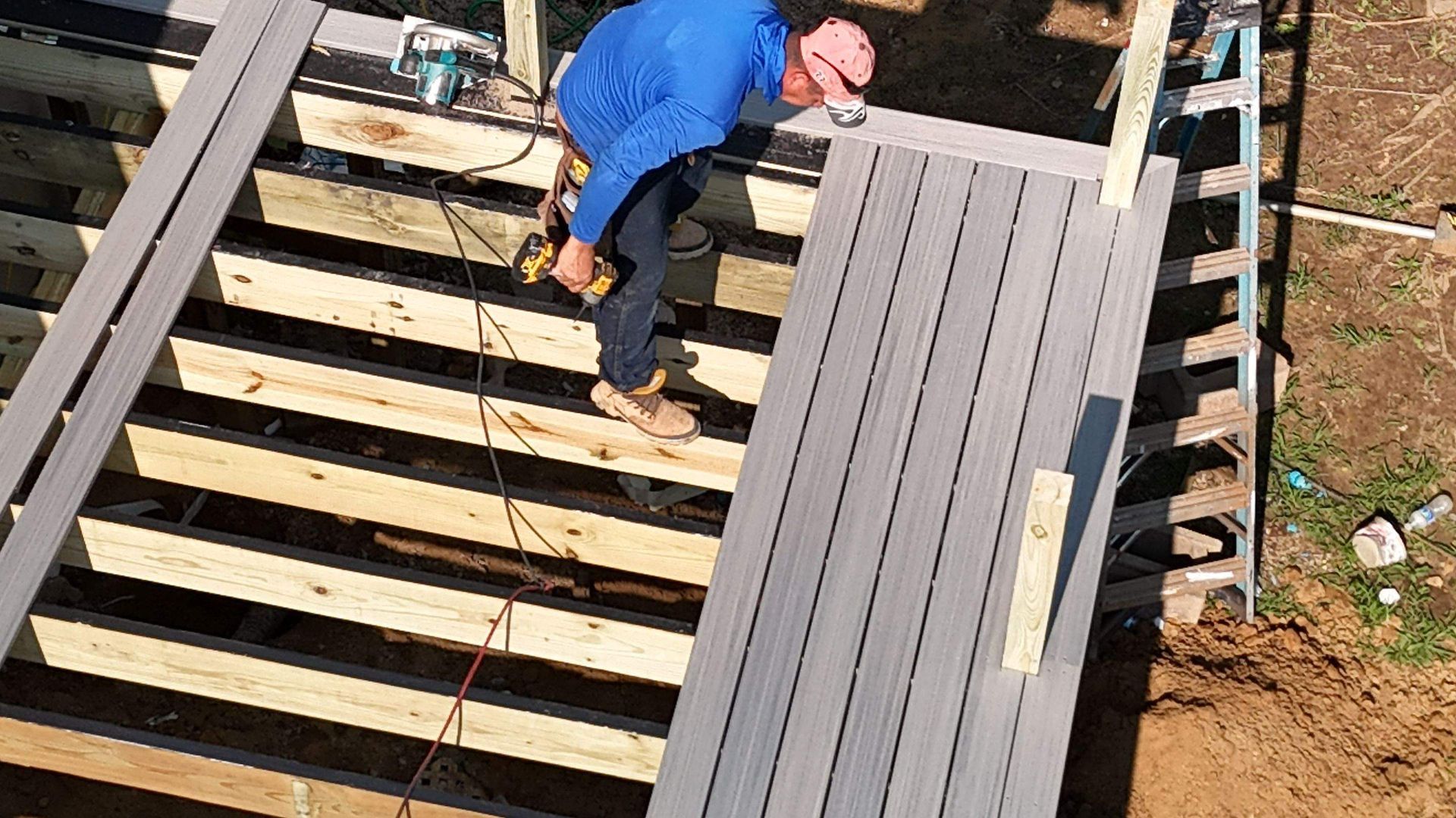 A man is working on a wooden deck with a drill.