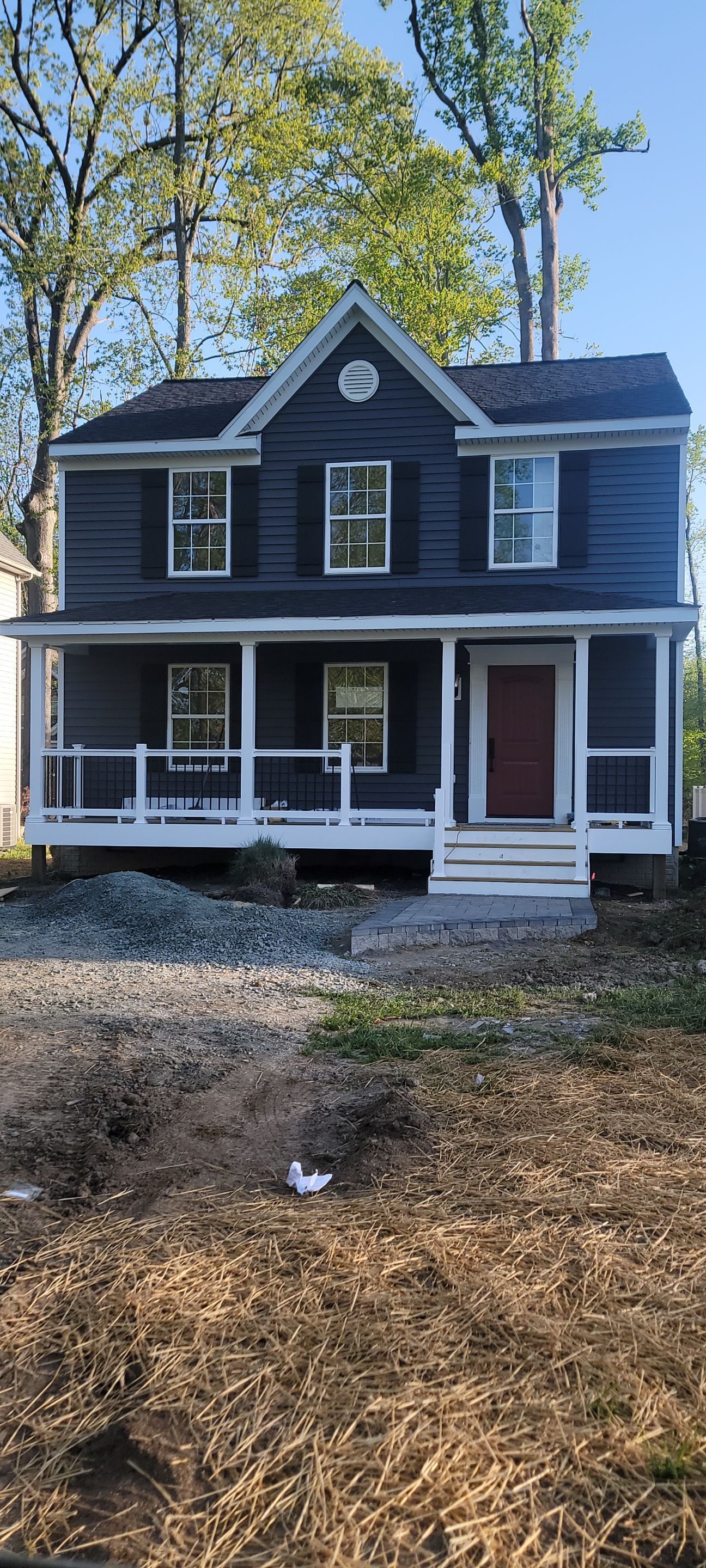 A large house with a large porch is sitting on top of a dirt field.