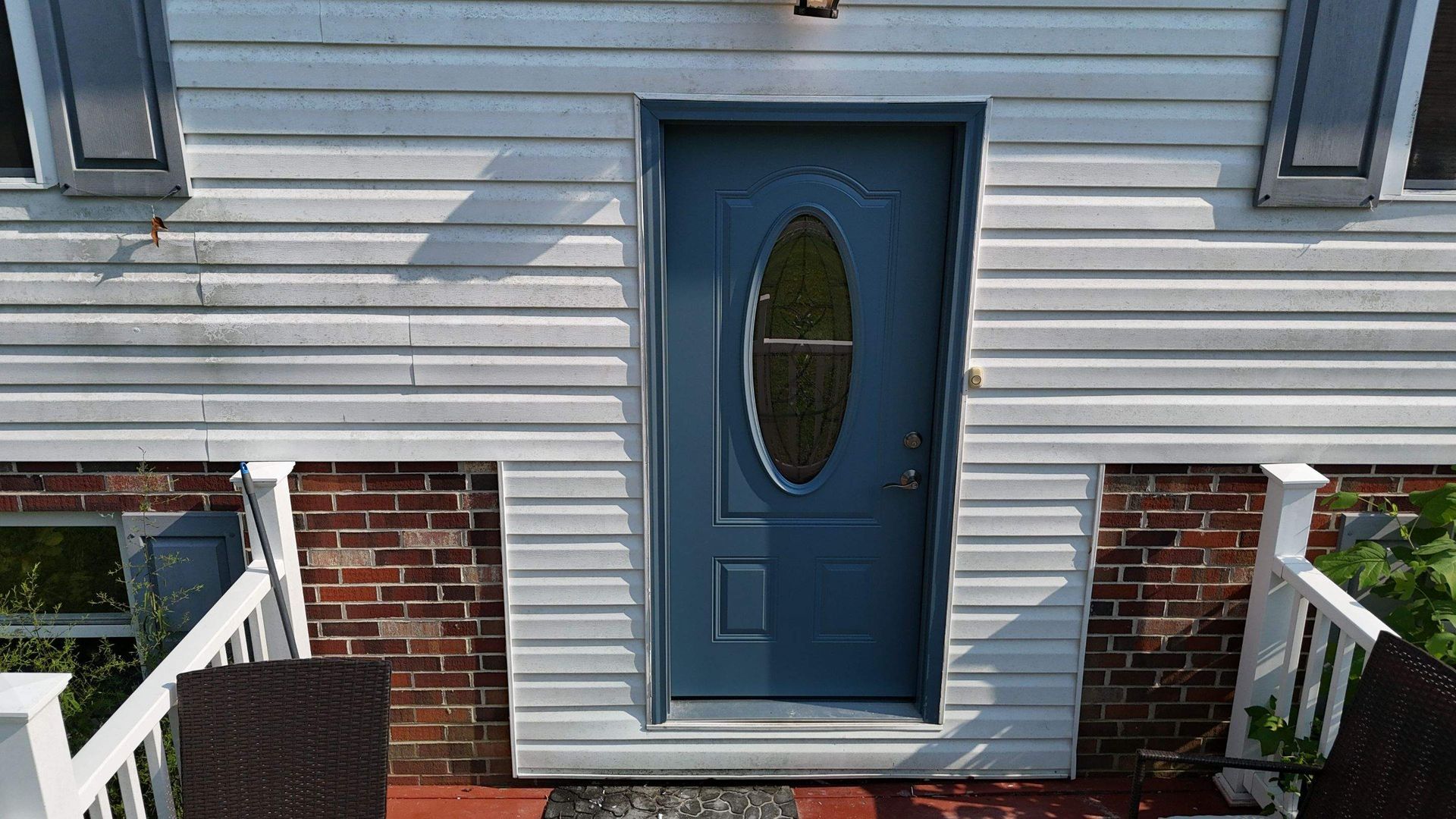 A blue door with an oval window is on the front of a white house.
