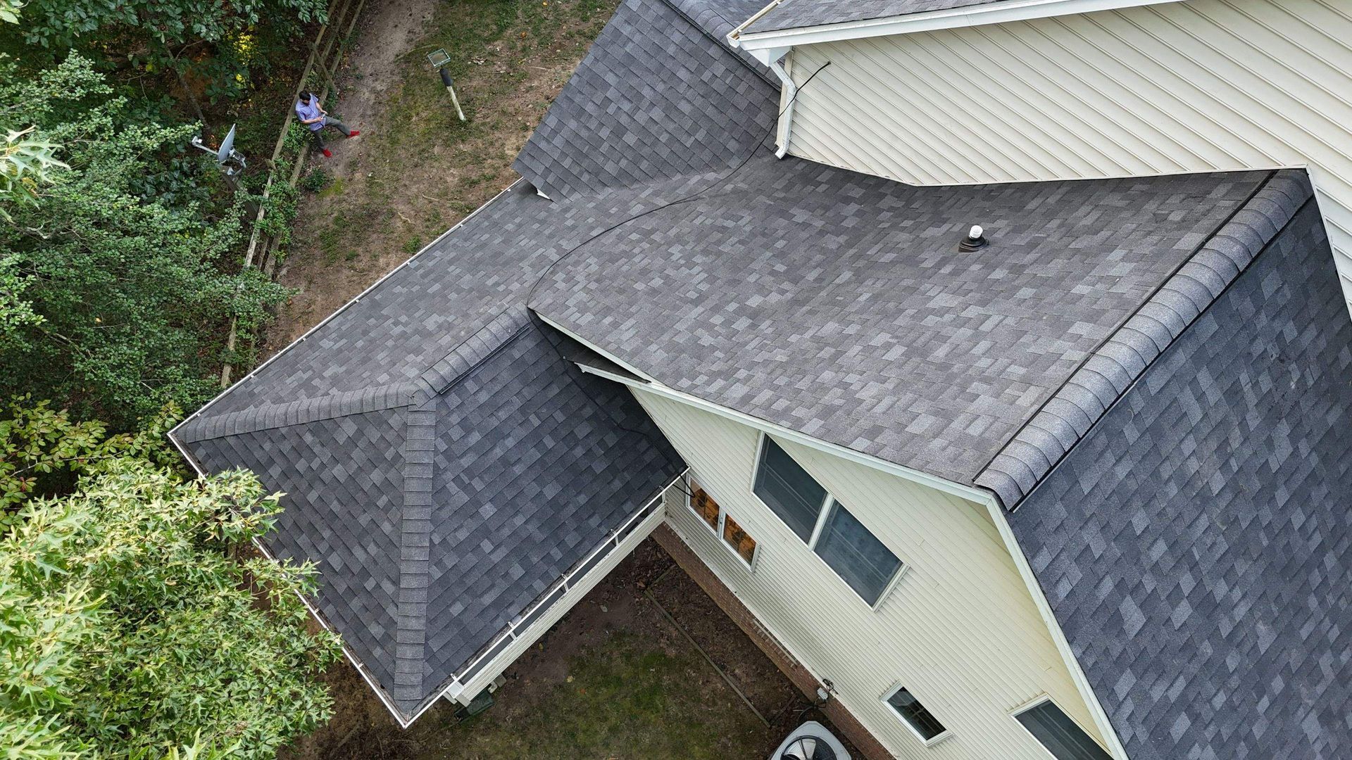 An aerial view of a house with a gray roof surrounded by trees.