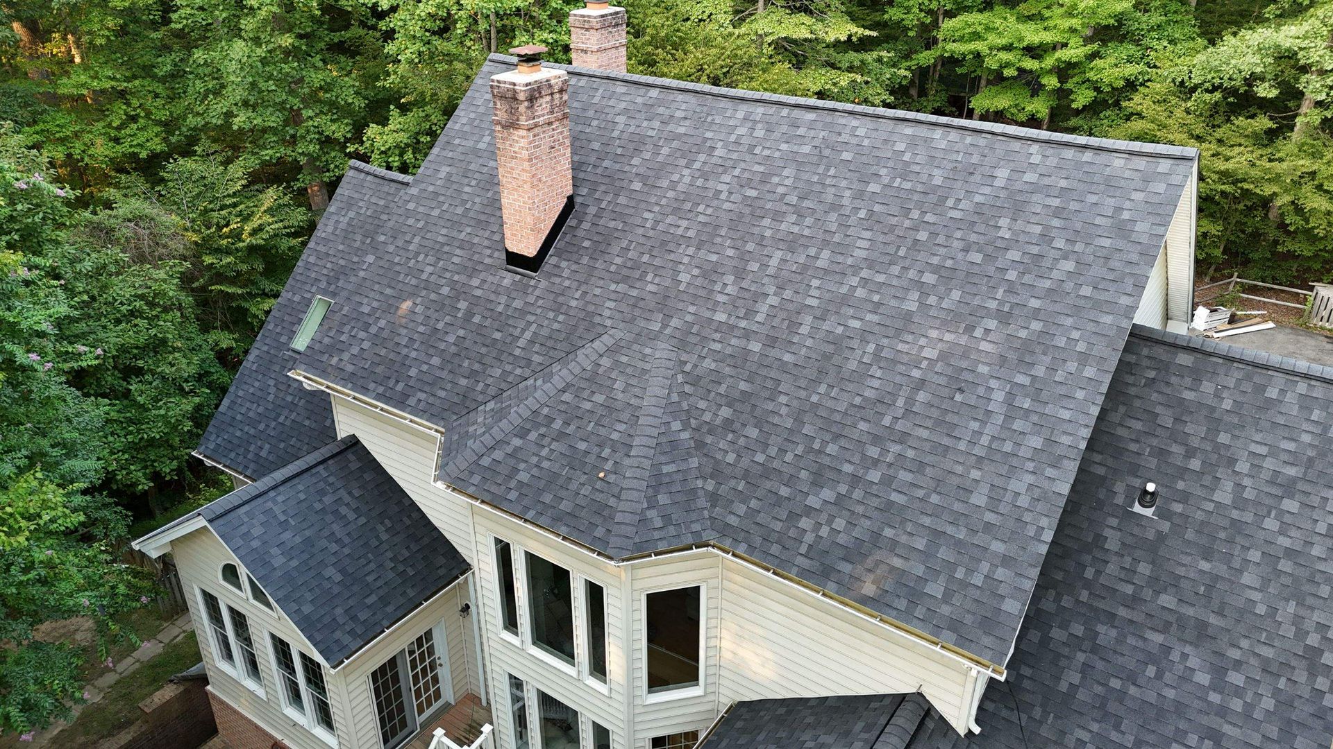 An aerial view of a large house with a black roof and a chimney.