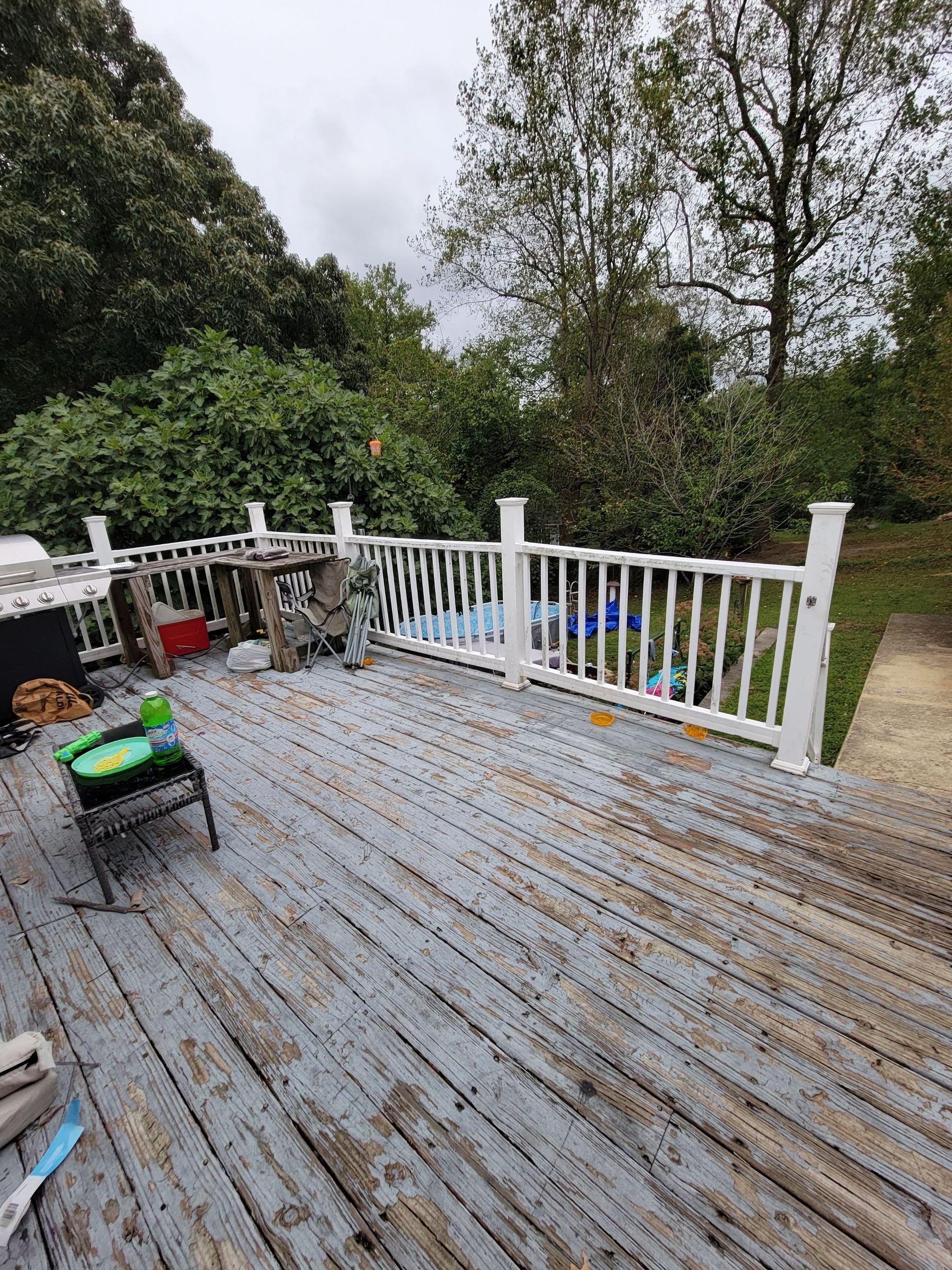 A wooden deck with a white railing and trees in the background.