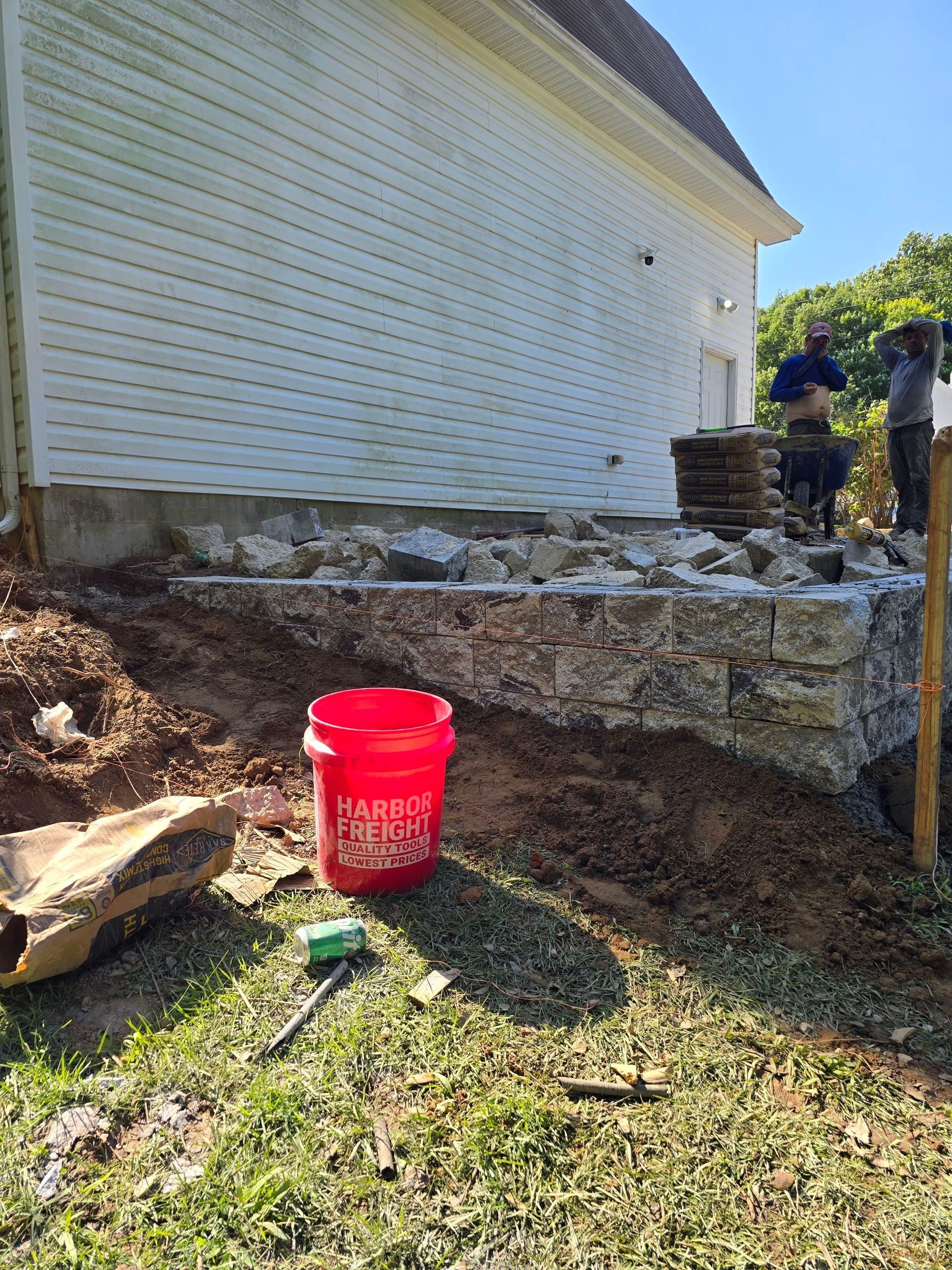 A red bucket is sitting in the grass in front of a house.