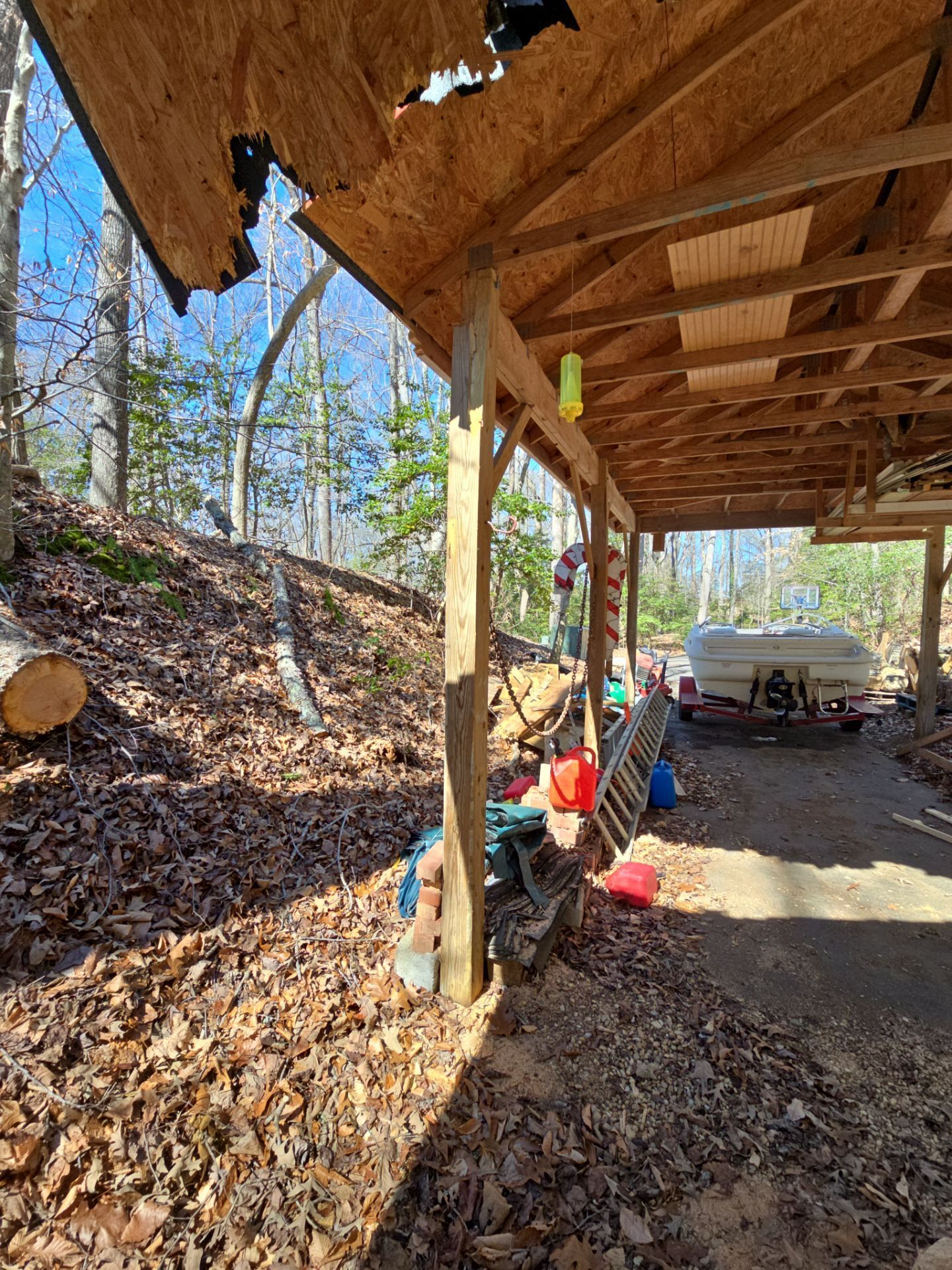 A boat is parked under a covered area in the woods.