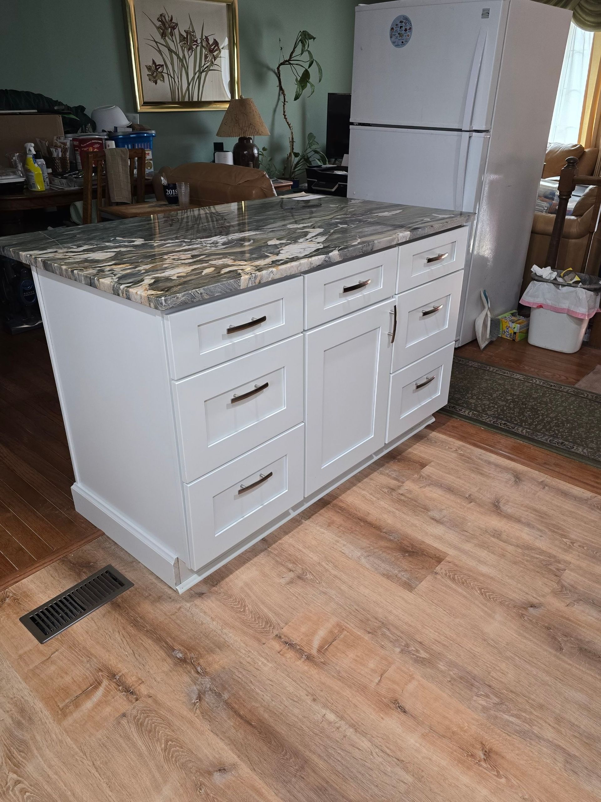 A kitchen island with drawers and a refrigerator in a living room.