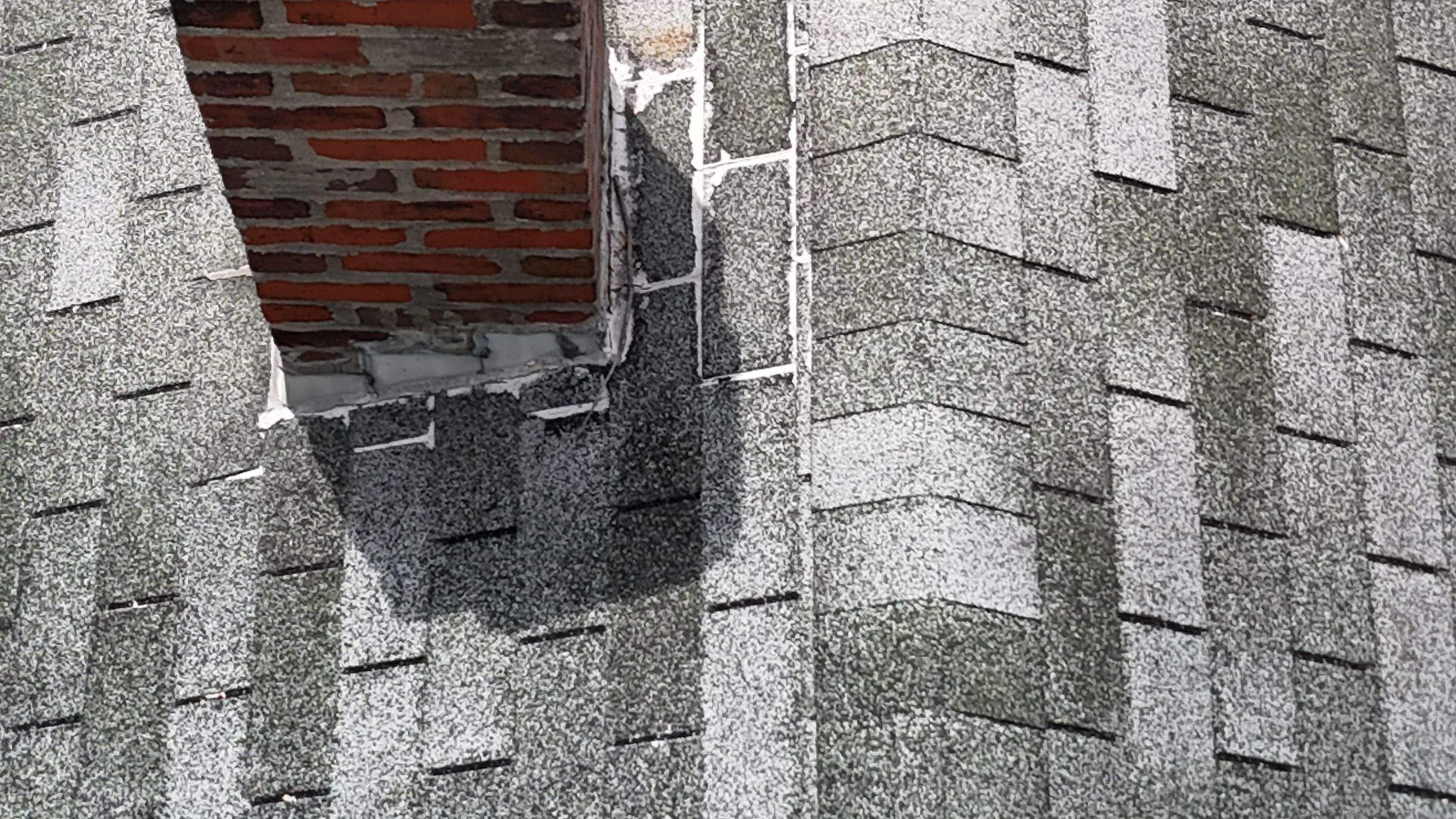 A roof with a hole in it and a brick chimney.