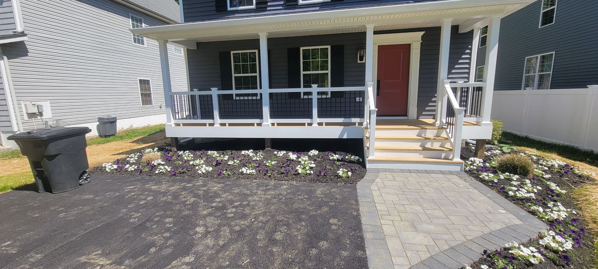 A house with a porch and a trash can in front of it.