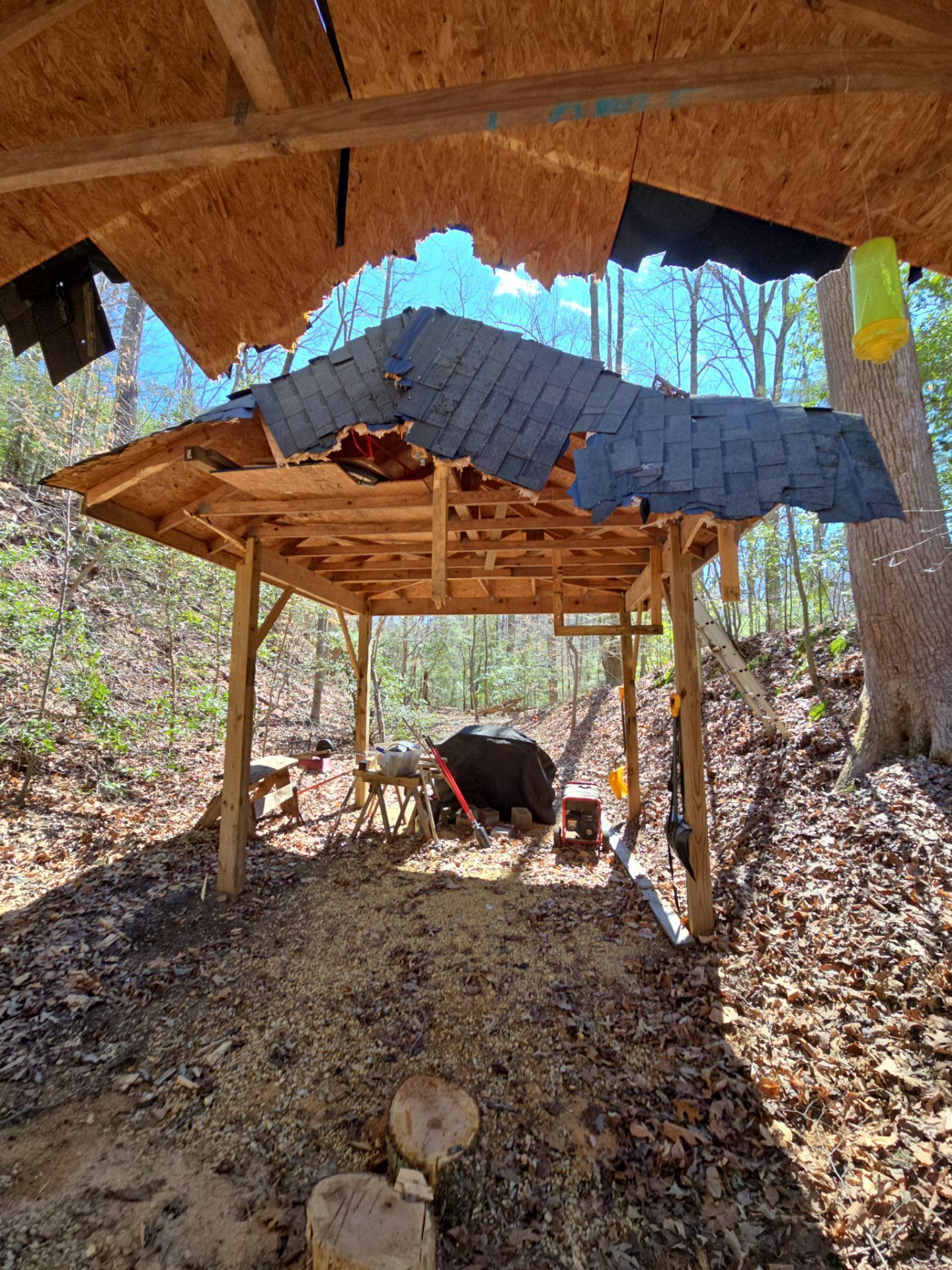 A wooden structure in the middle of a forest with a roof that is missing.