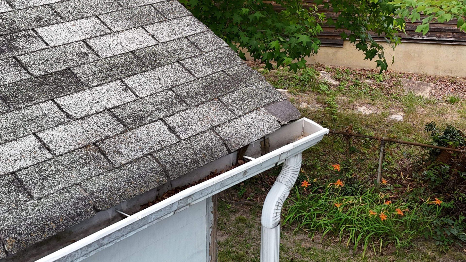 A gutter on the side of a house next to a roof.