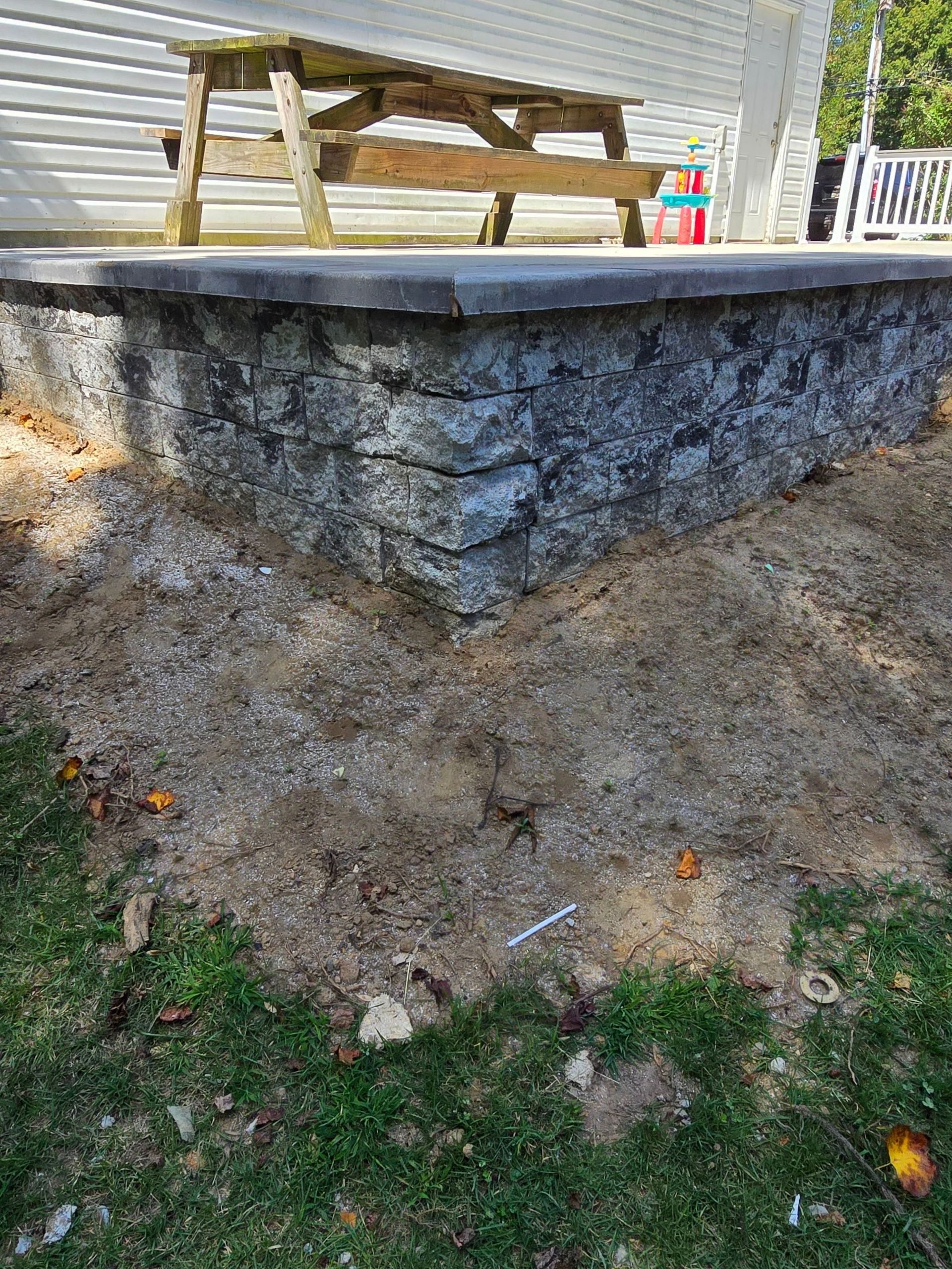 A stone wall is being built next to a wooden picnic table.