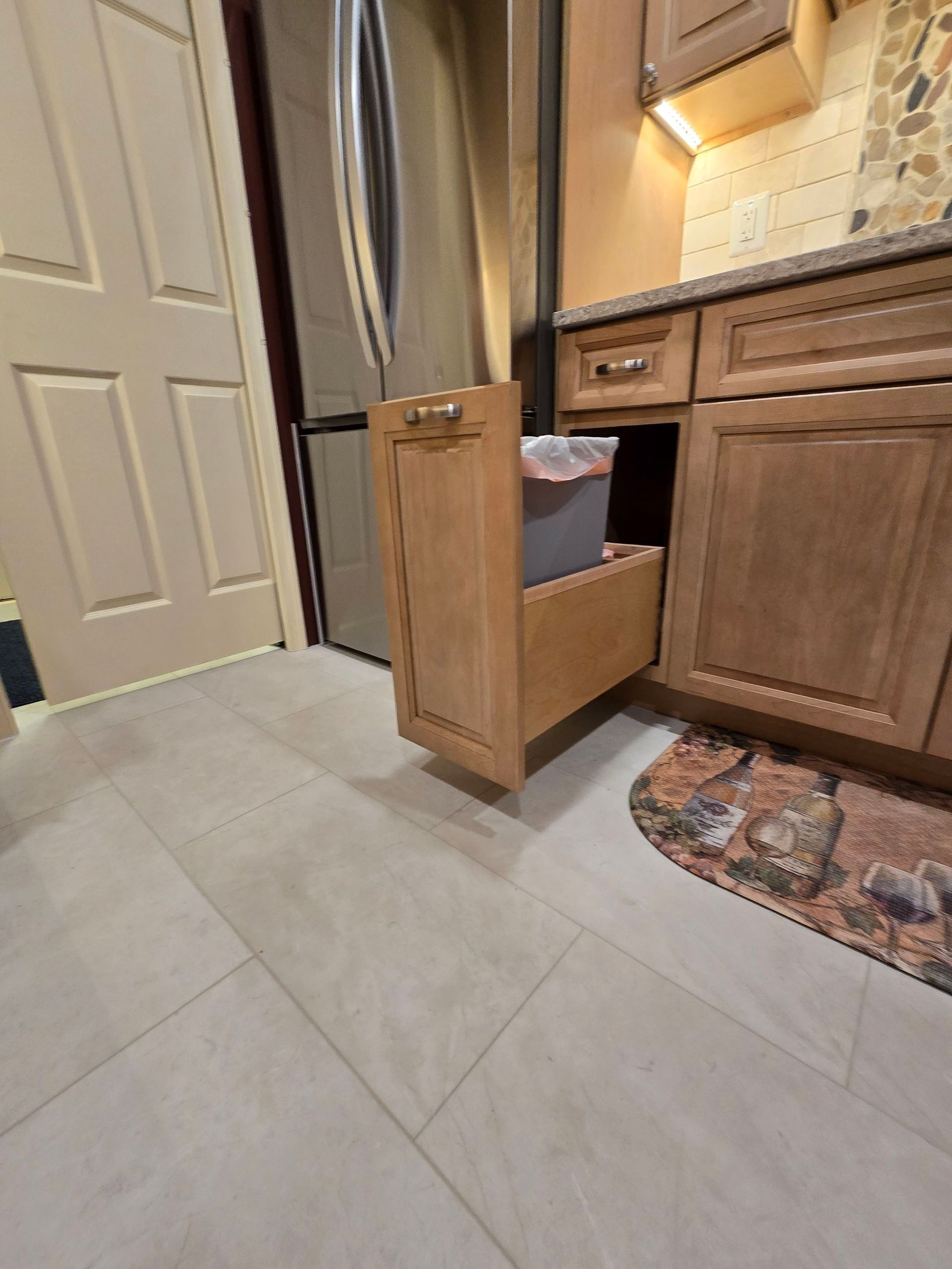 A kitchen with wooden cabinets and a drawer with a trash can in it.