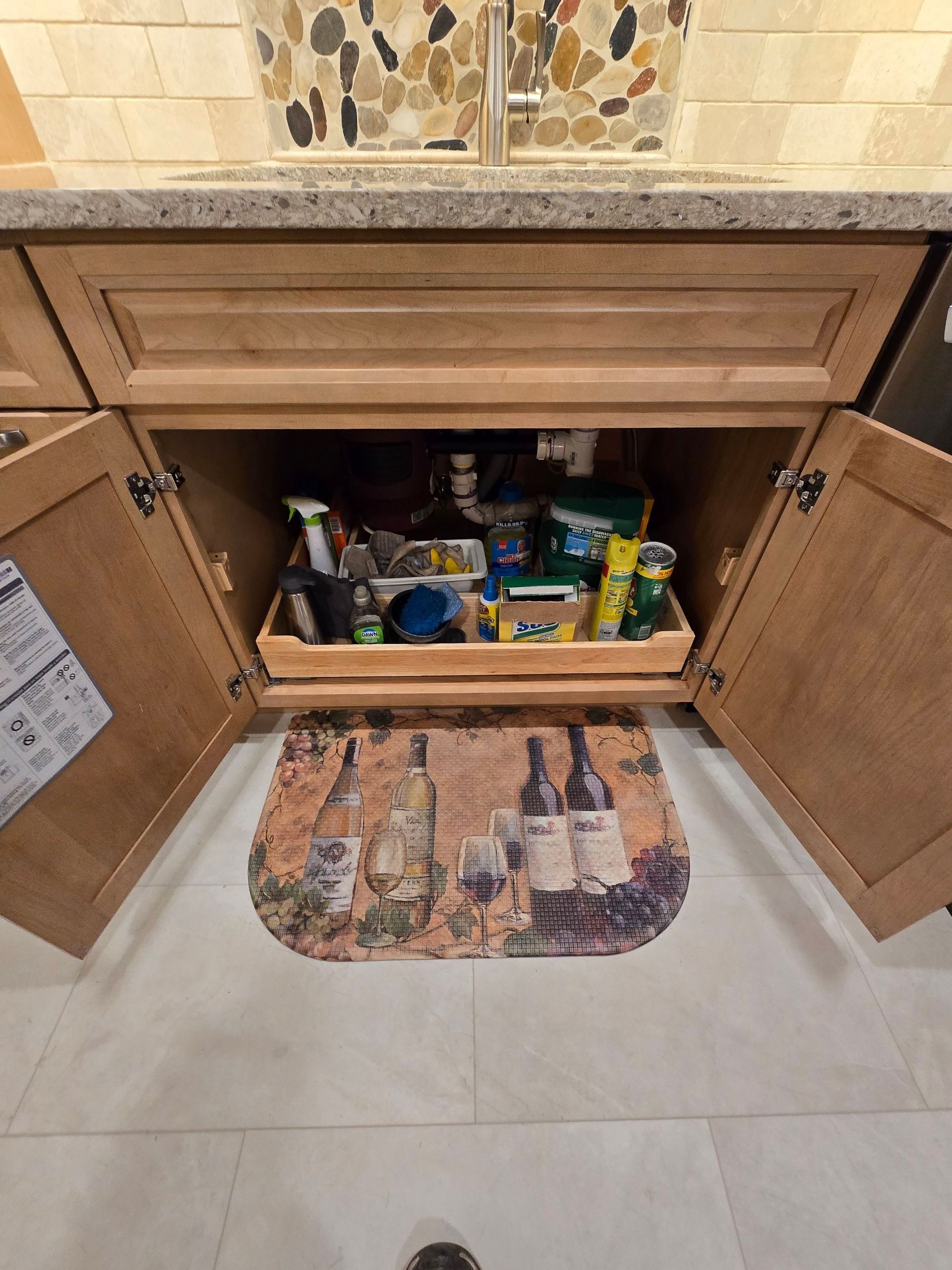 A kitchen sink with a tray of cleaning supplies underneath it.