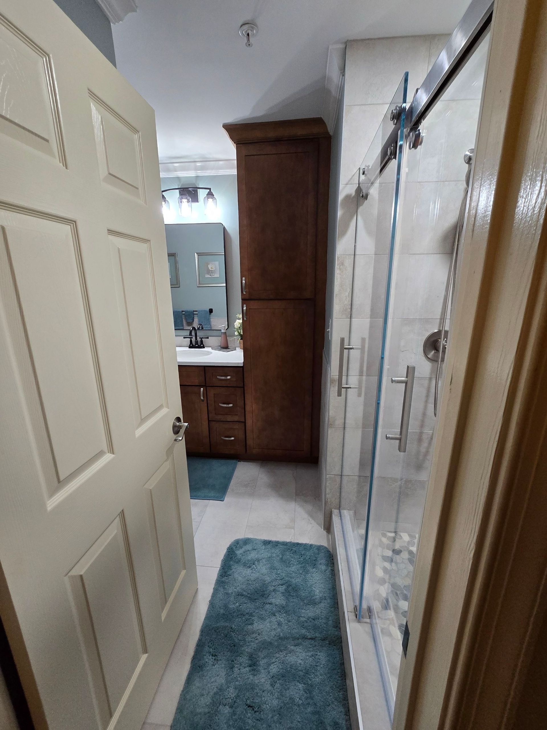 A bathroom with a sliding glass shower door and a blue rug.