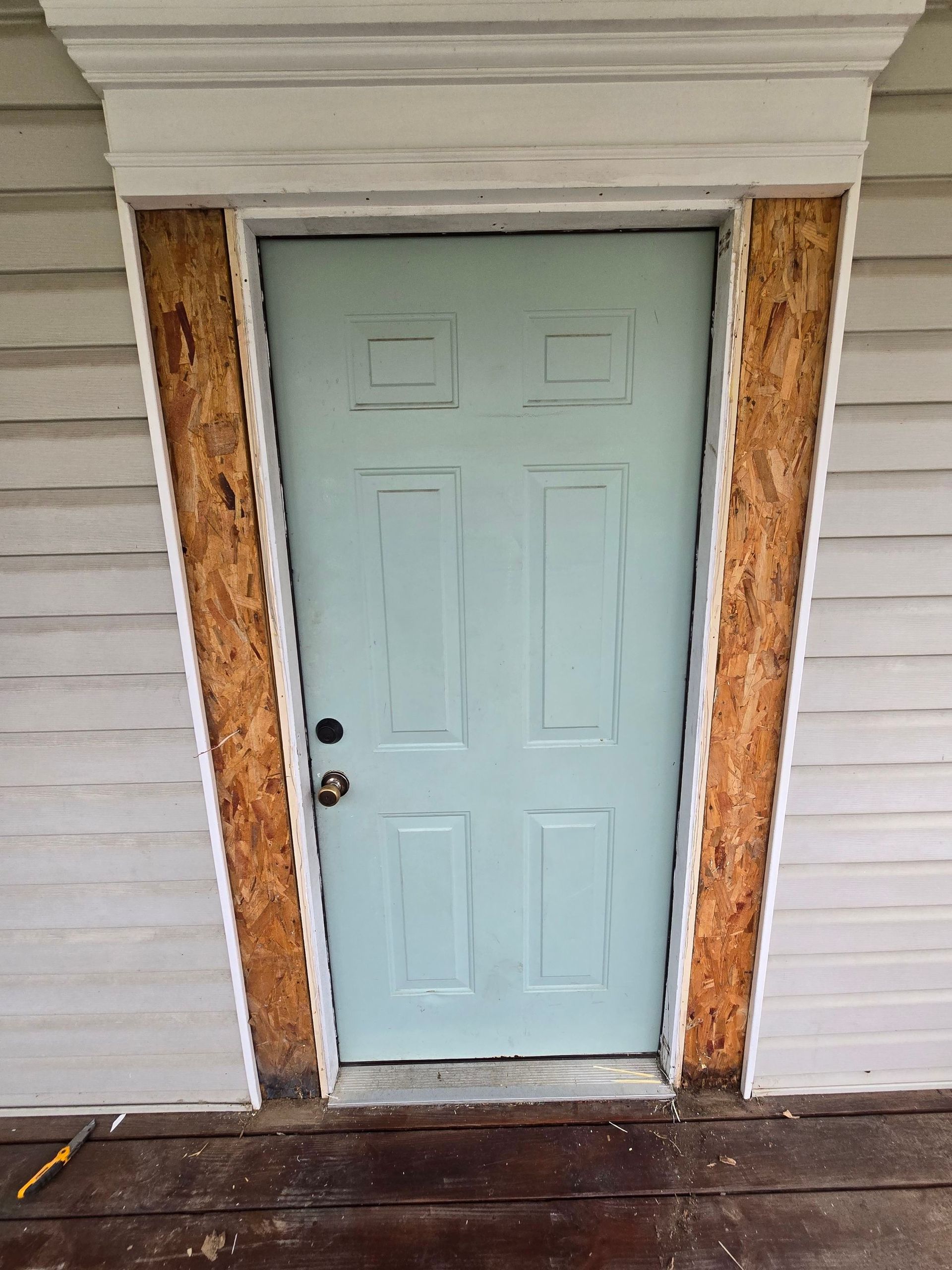 A light blue door is sitting on a wooden porch.