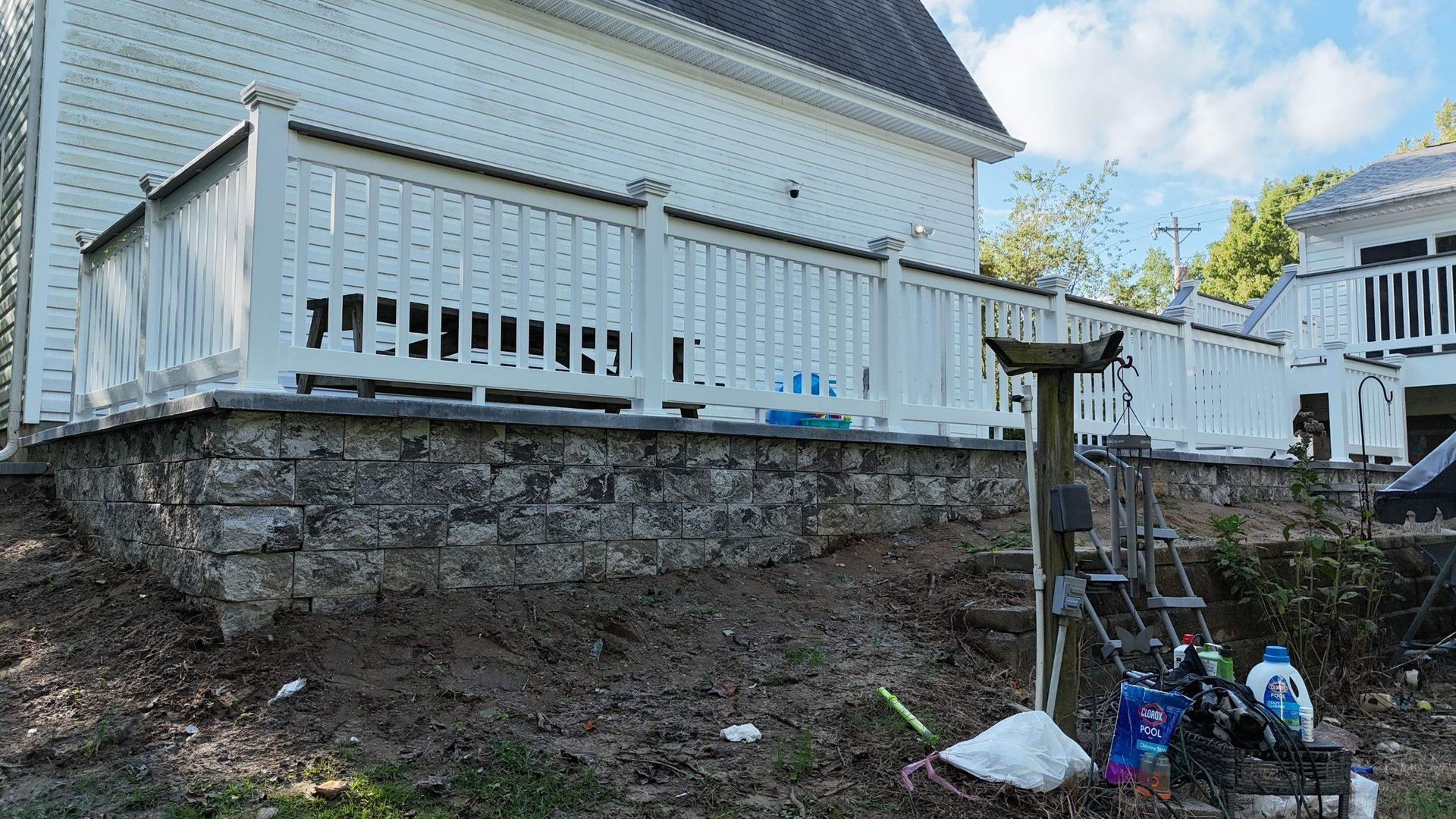 A white house with a white deck and a stone wall.
