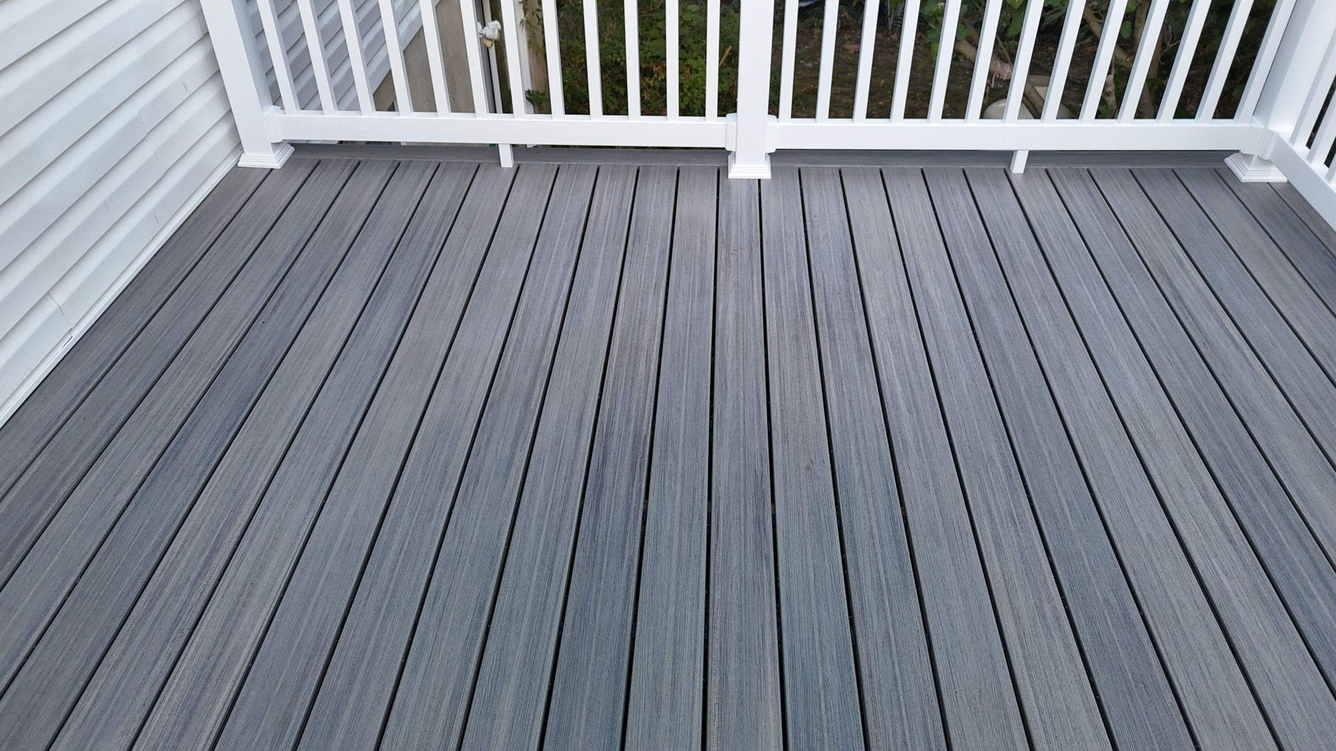 A gray deck with a white railing and a white house in the background.