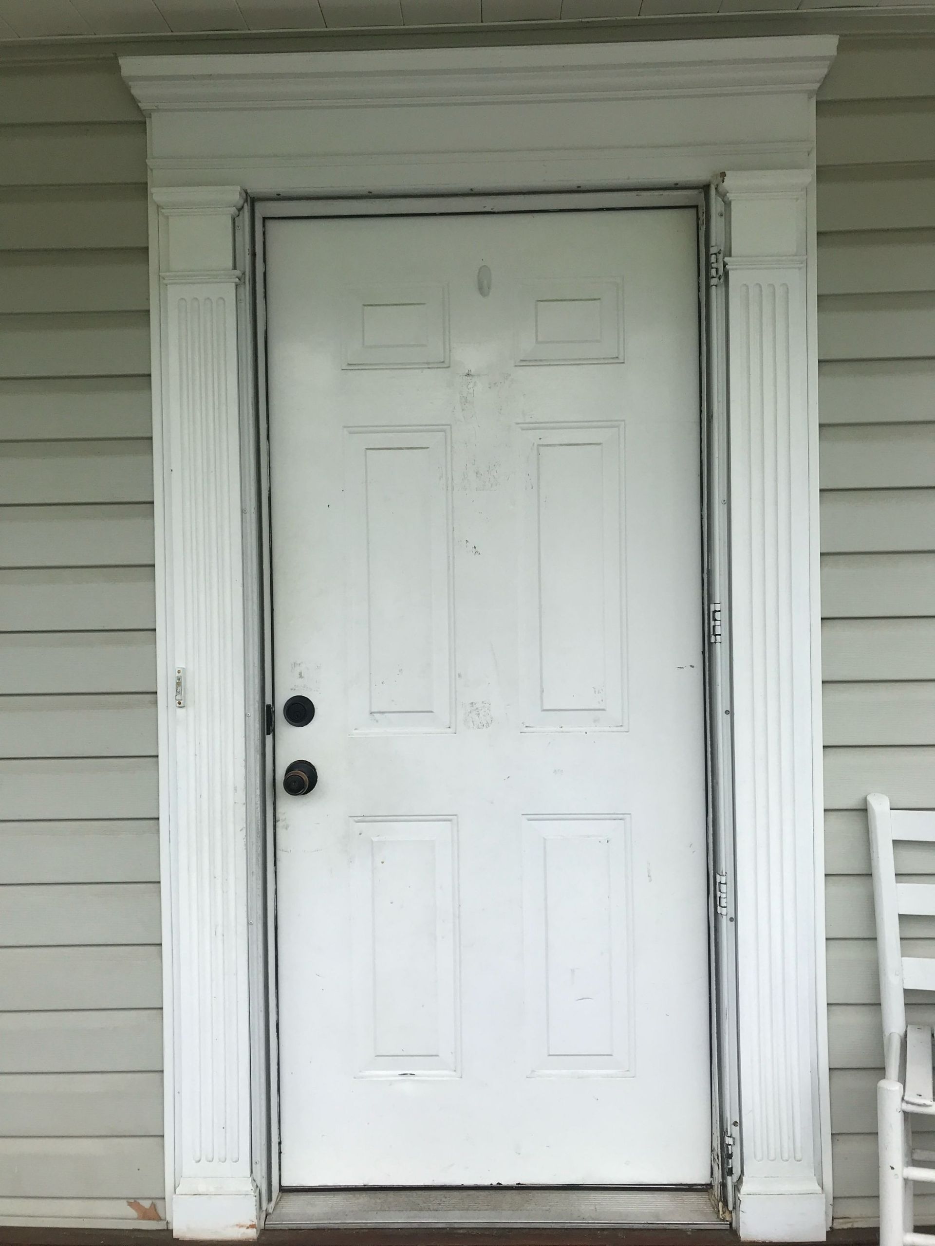A white door on a house with a rocking chair in front of it