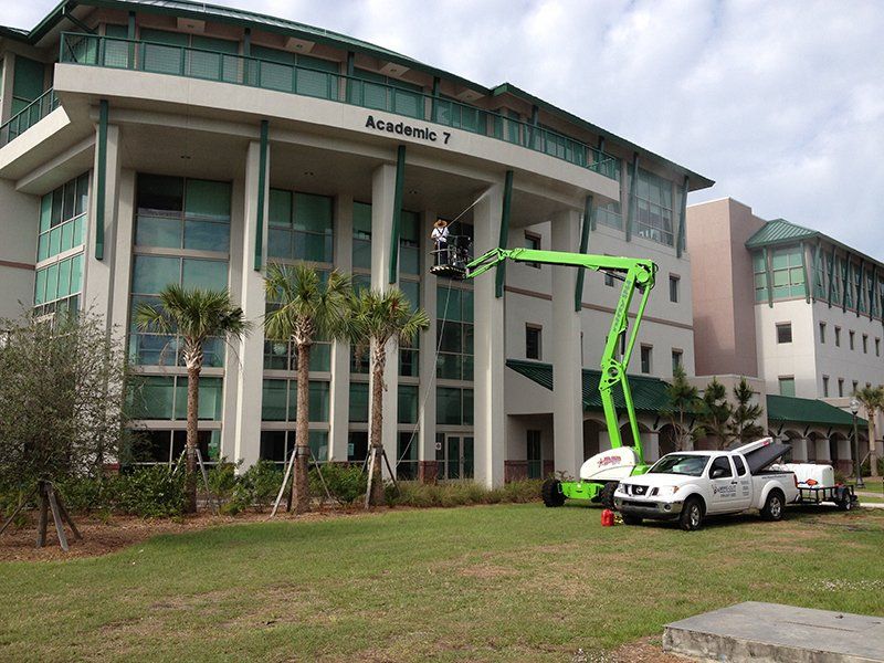 Man Cleaning Commercial Building Using Pressure Washer — Fort Myers, FL — Wipe Out Windows