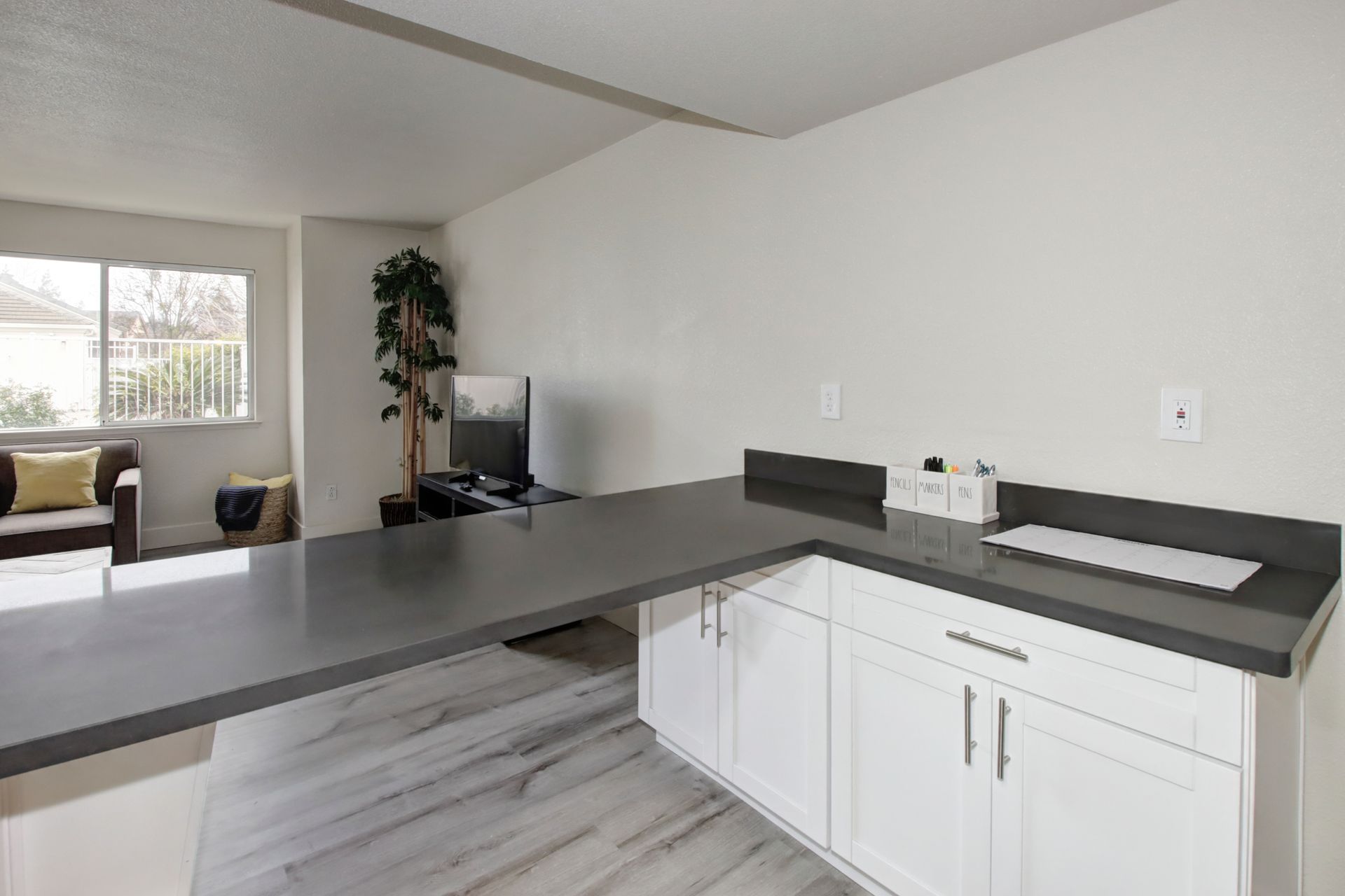 White cabinets with a gray countertop, a computer, and a window.