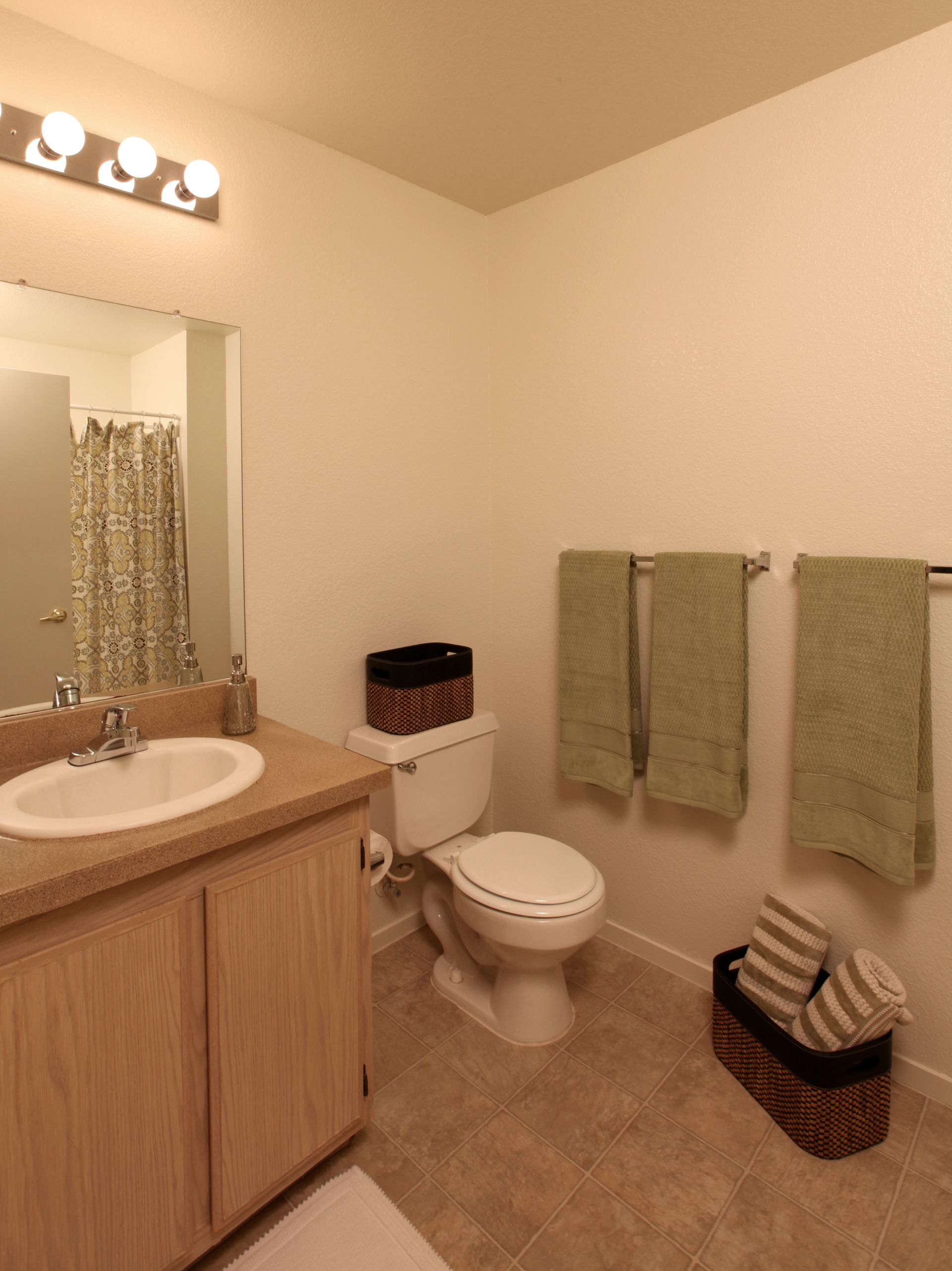 Bathroom with light-colored walls, beige flooring, toilet, vanity, mirror, and green towels.