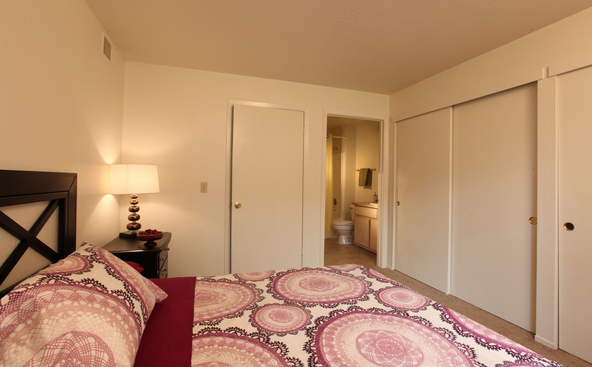 Bedroom with bed, nightstand, closet, and doorway to a bathroom. Bed has patterned comforter.