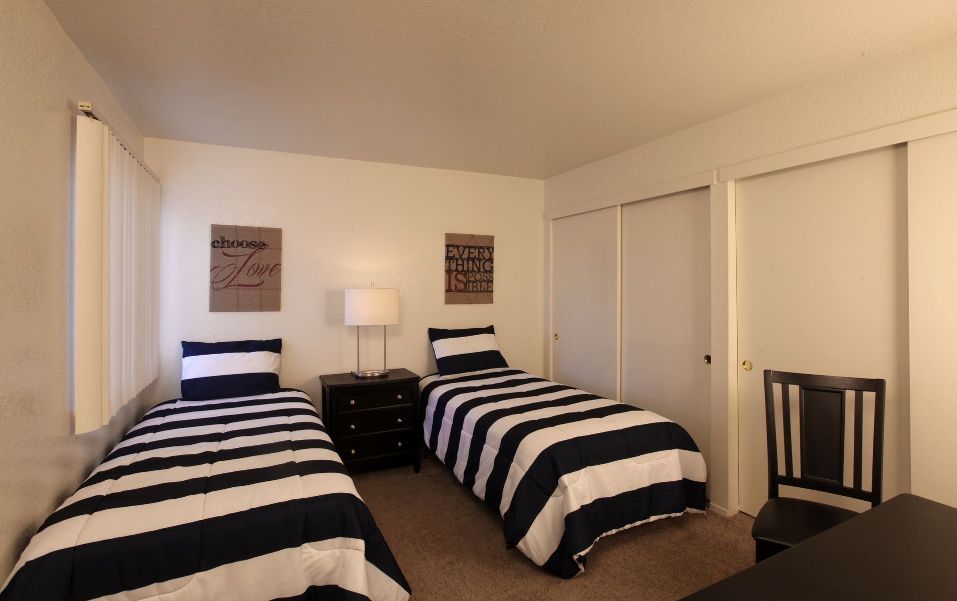 Two twin beds with navy and white striped bedding in a bedroom with white walls and a black desk.