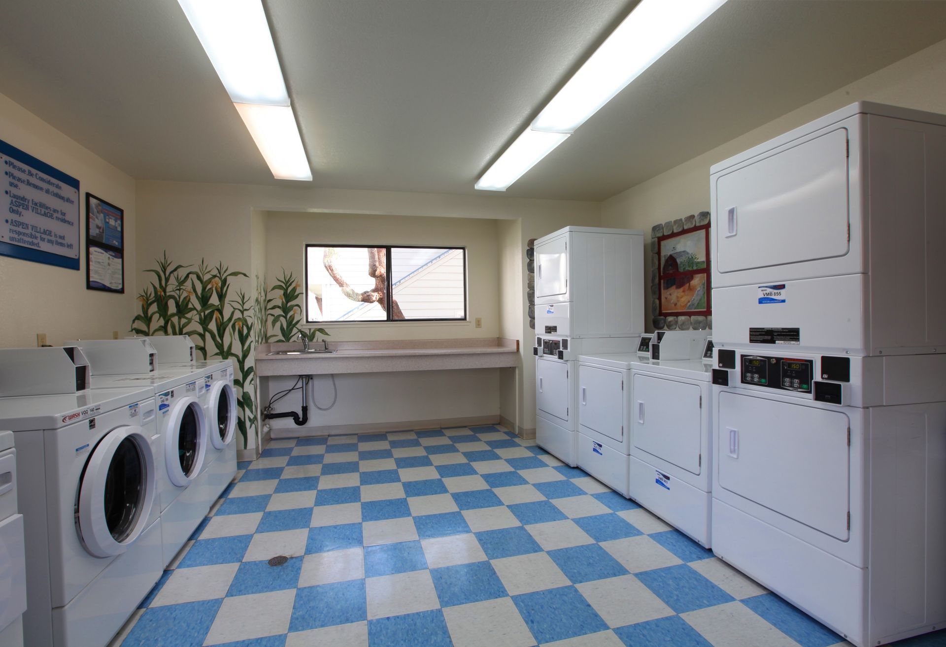 Laundry room with white washers and dryers, blue and white checkered floor, and a window.