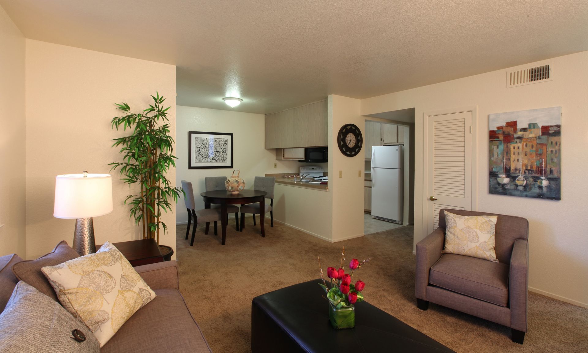Living room with brown sofa, armchair, dining table, and kitchen visible.