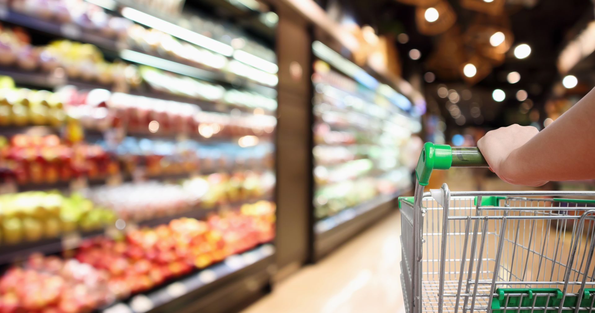 photo of a shopping cart being pushed through the produce section in a grocery store