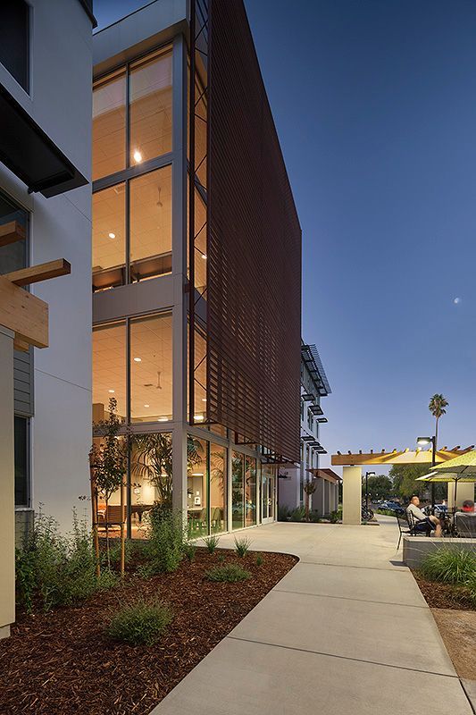 Modern building exterior with tall windows, brown lattice, and a walkway at dusk.