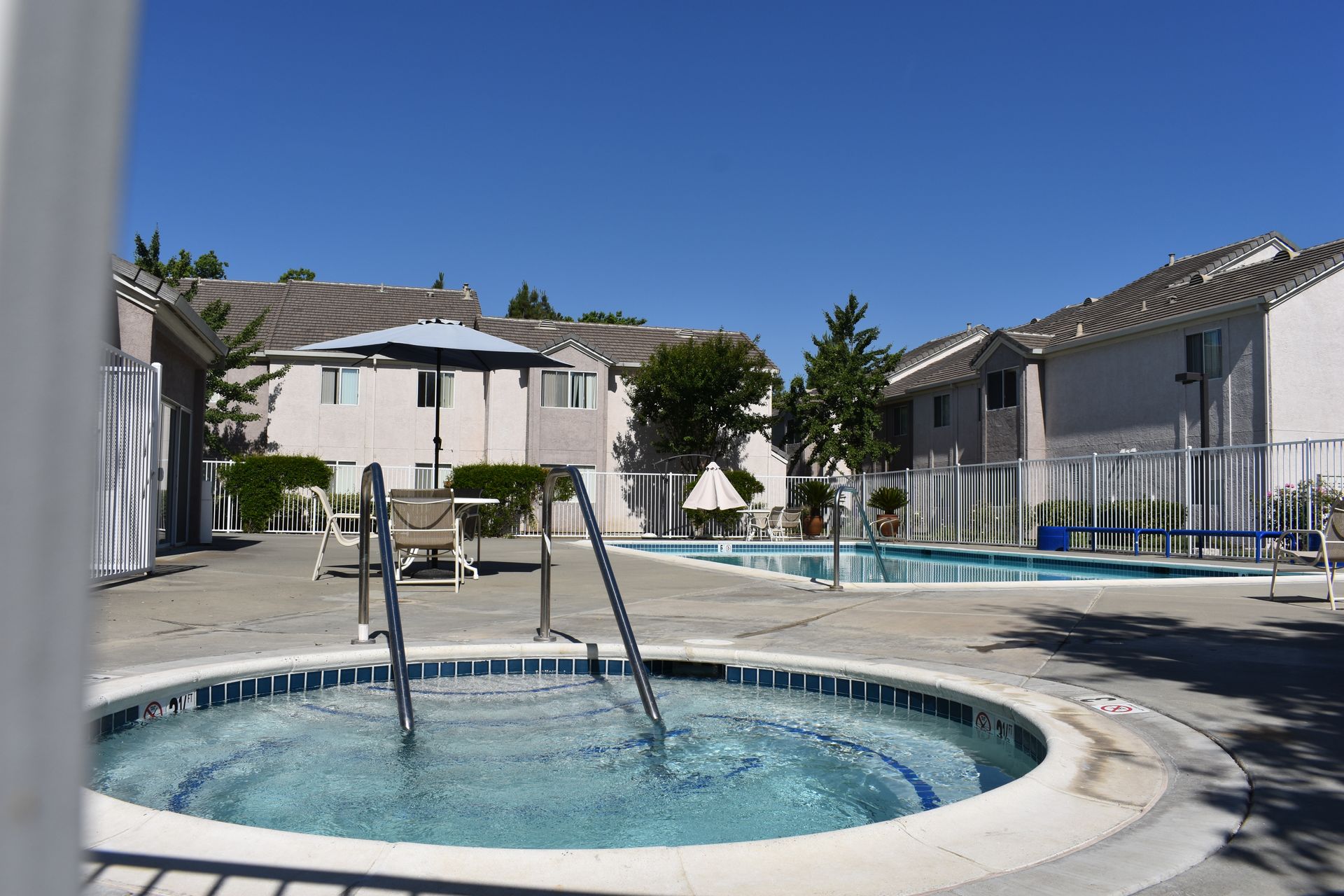 A hot tub and pool with buildings in the background on a sunny day.