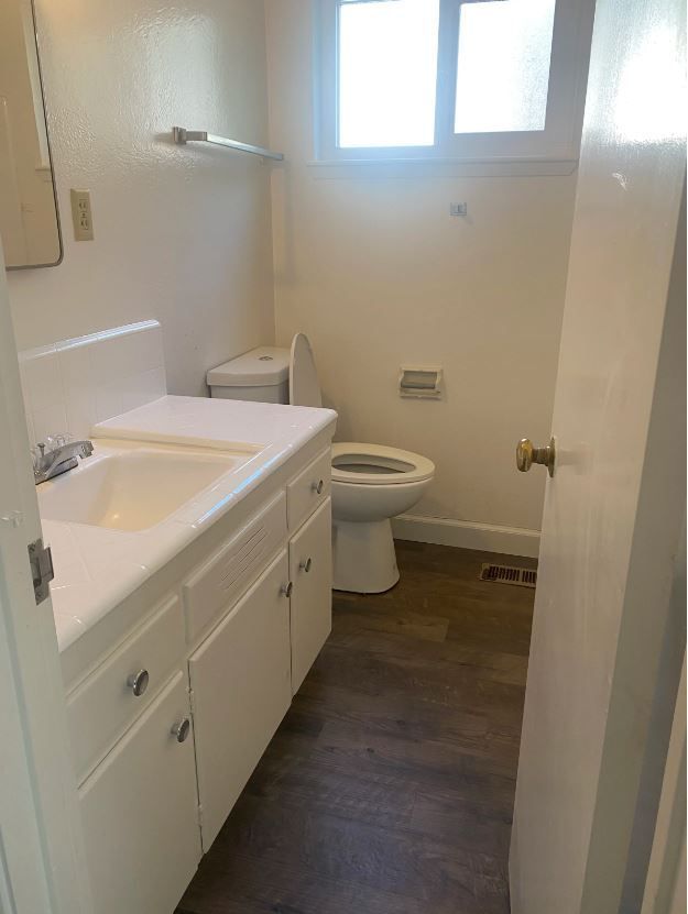 Bathroom with white fixtures, vanity, toilet, and a small window; dark flooring.
