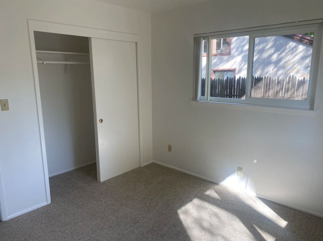Empty bedroom with closet, closed door, window, and carpet.
