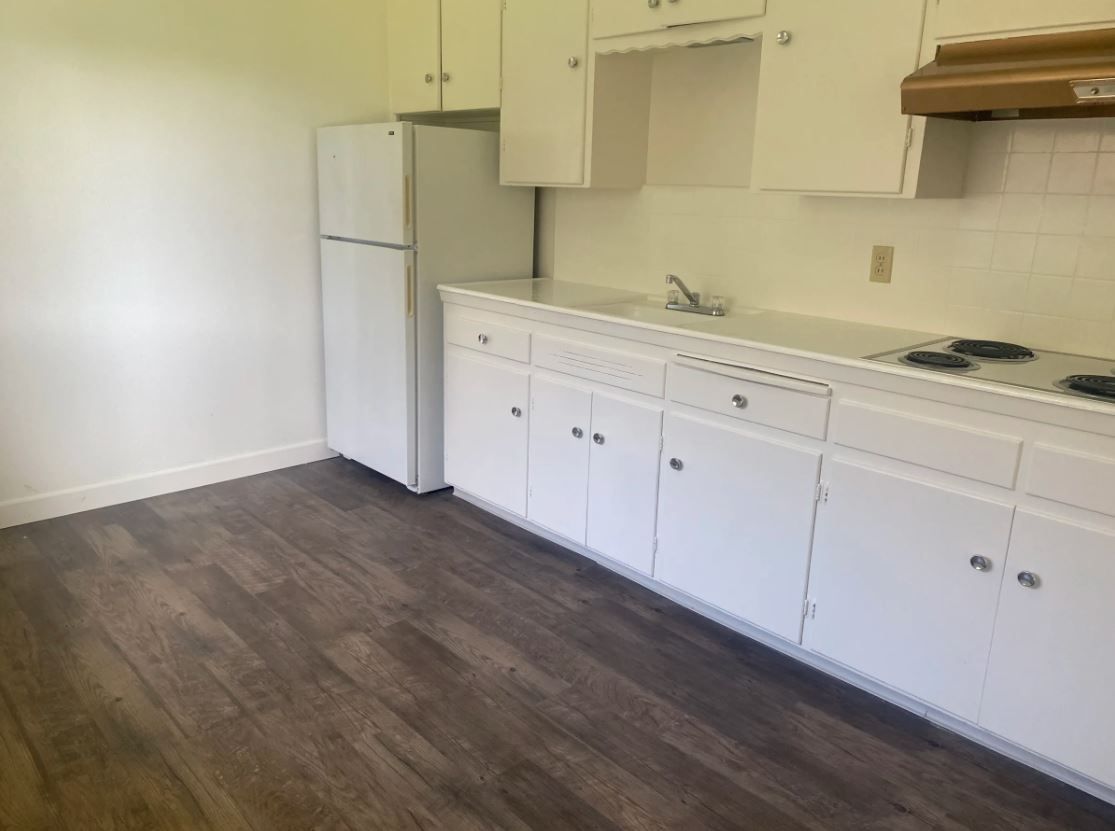 Kitchen with white cabinets, a refrigerator, and a stove with dark wood-look flooring.