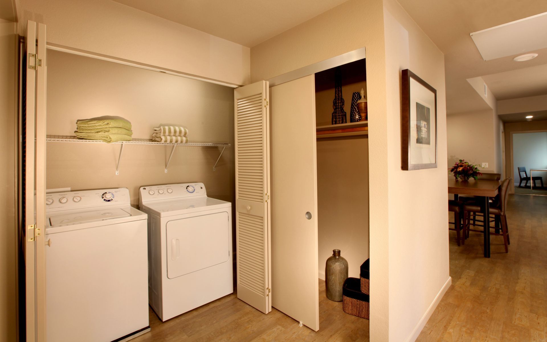 Laundry room with washer, dryer, shelves with towels, and adjacent storage closet.