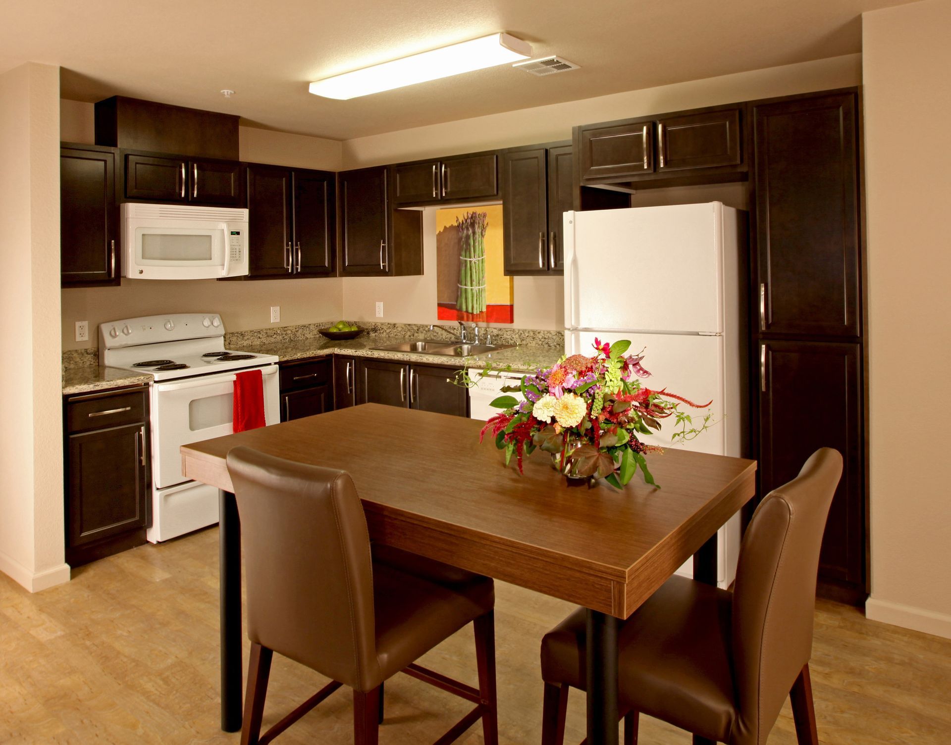 Kitchen with dark cabinets, white appliances, square table, and two chairs.