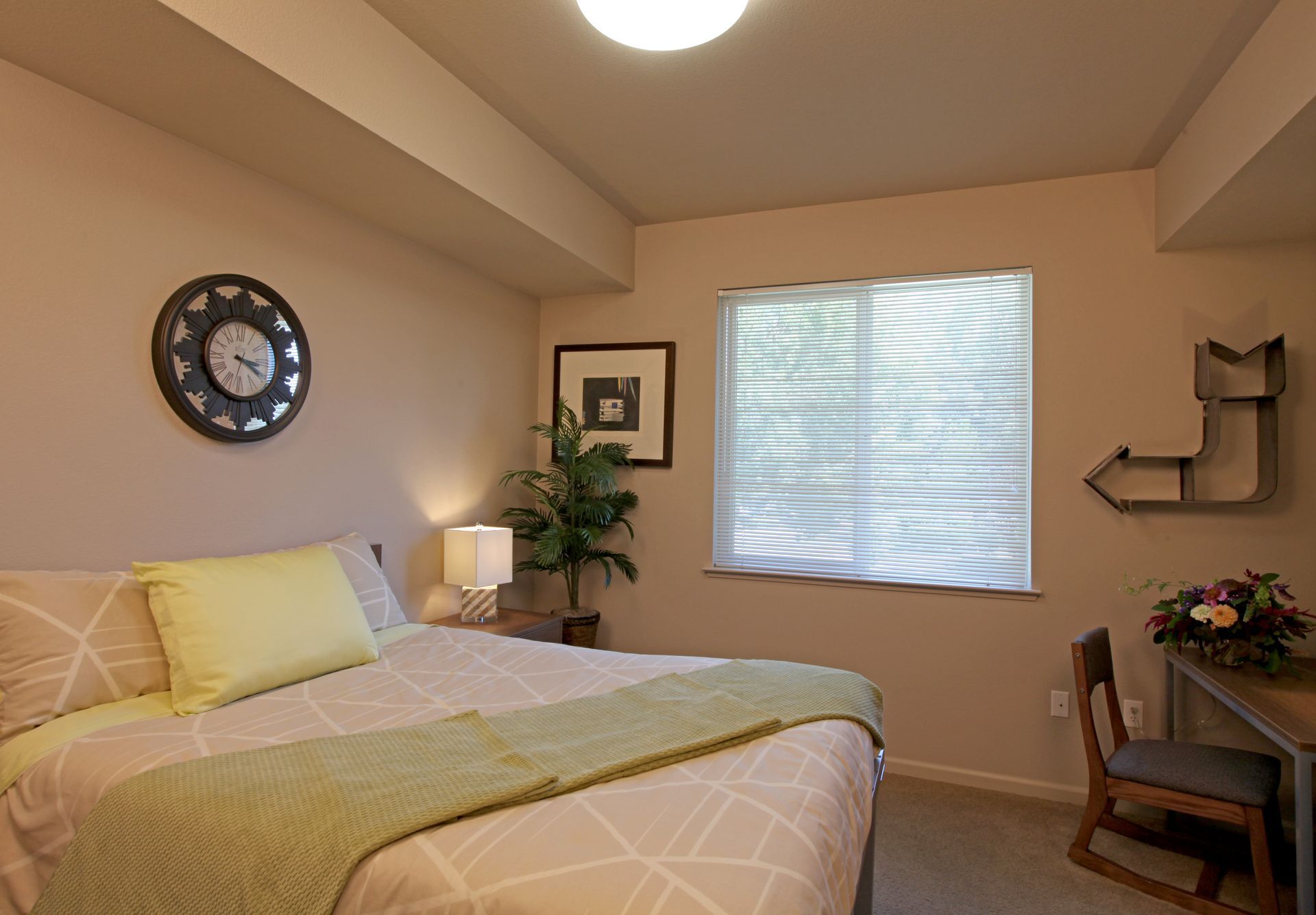 Bedroom with bed, clock, desk, window, and a plant. Cream walls with pale green accents.