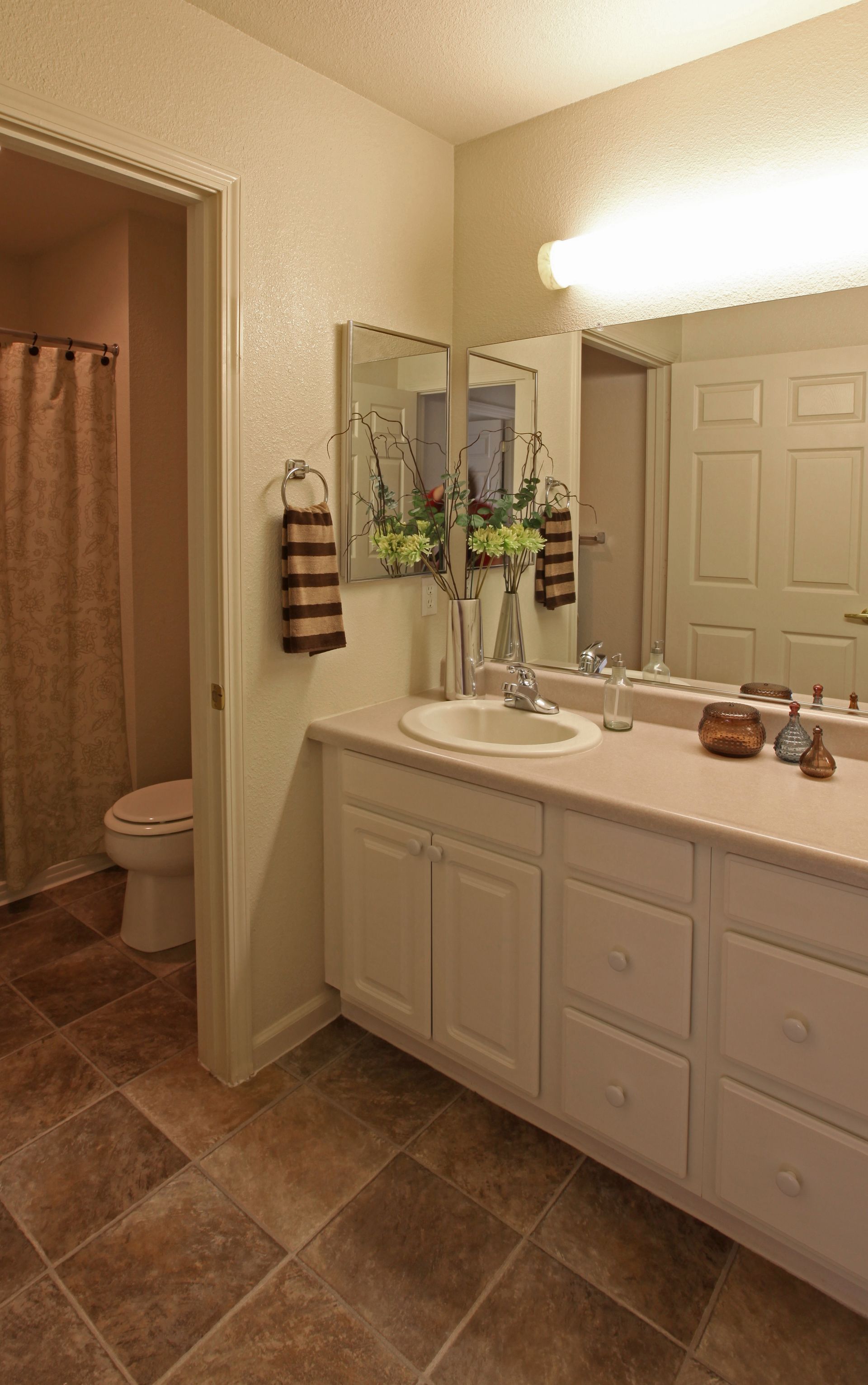 Bathroom with white cabinets, light-colored countertop, sink, and a toilet in an adjacent room.