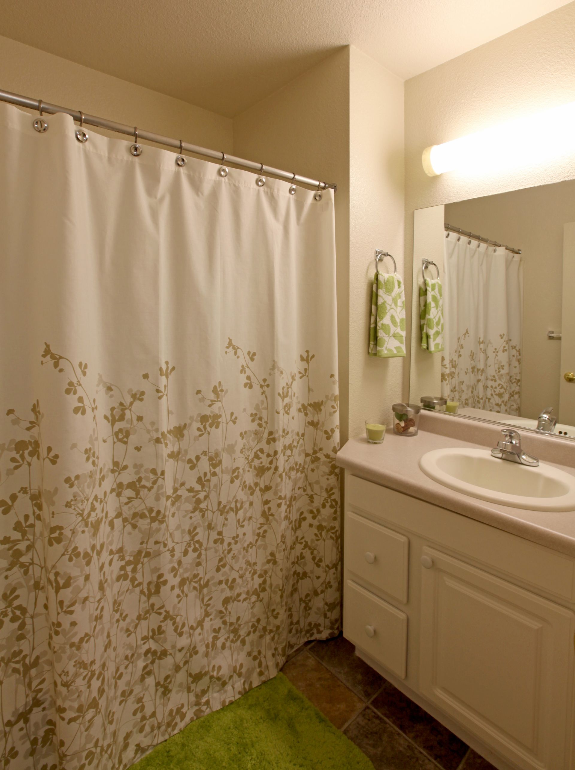 Bathroom with white vanity, beige walls, floral shower curtain, and green rug.
