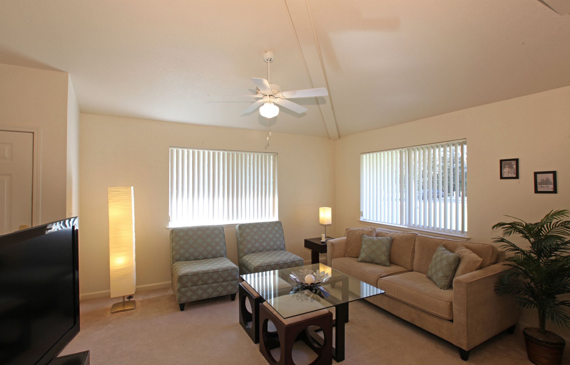 Beige living room with sofa, chairs, coffee table, blinds, and TV.