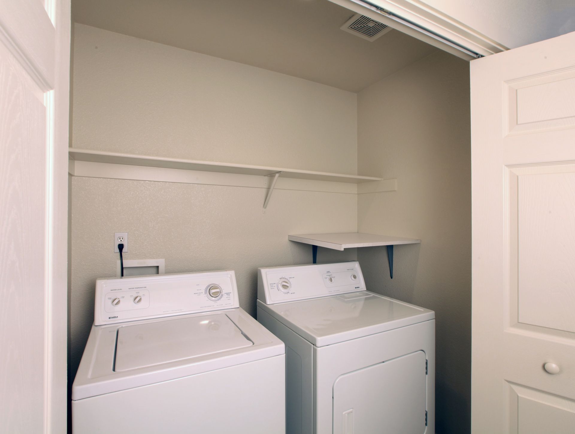 Laundry room with white washer and dryer, shelves, and open door.