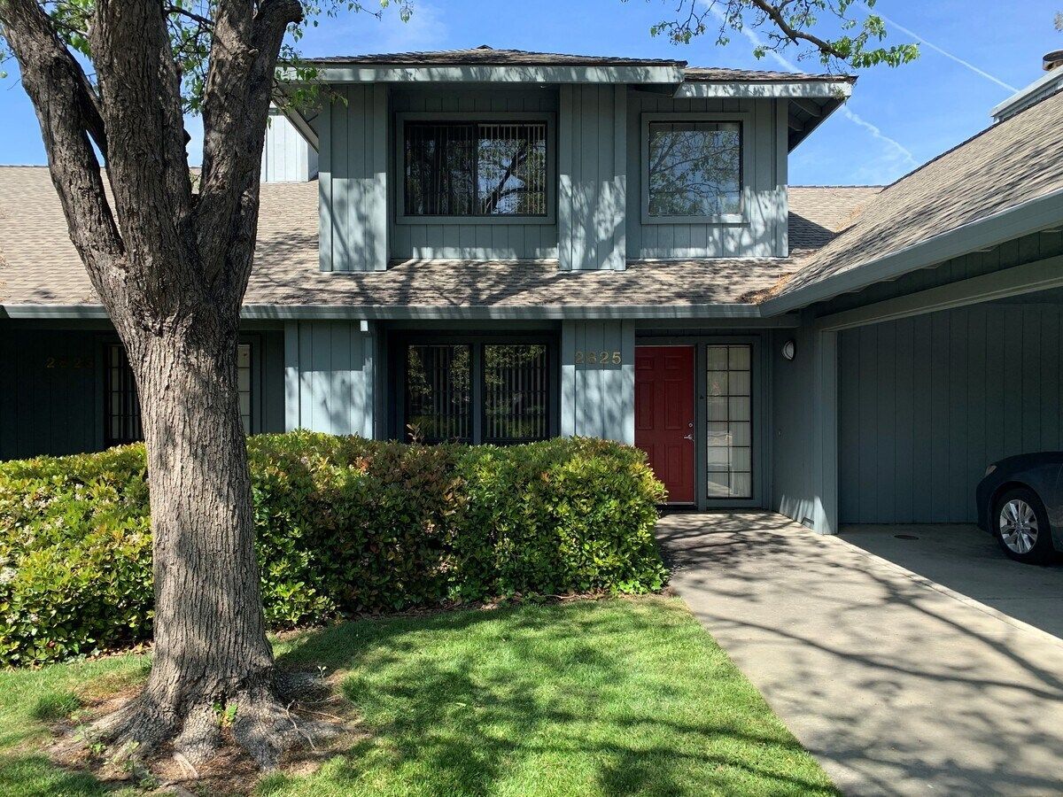 Blue two-story house with red door, windows, and a tree in front, on a sunny day.