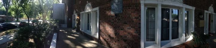 Building with windows covered in vines, shadowed pathway, bright sunlight, and greenery.