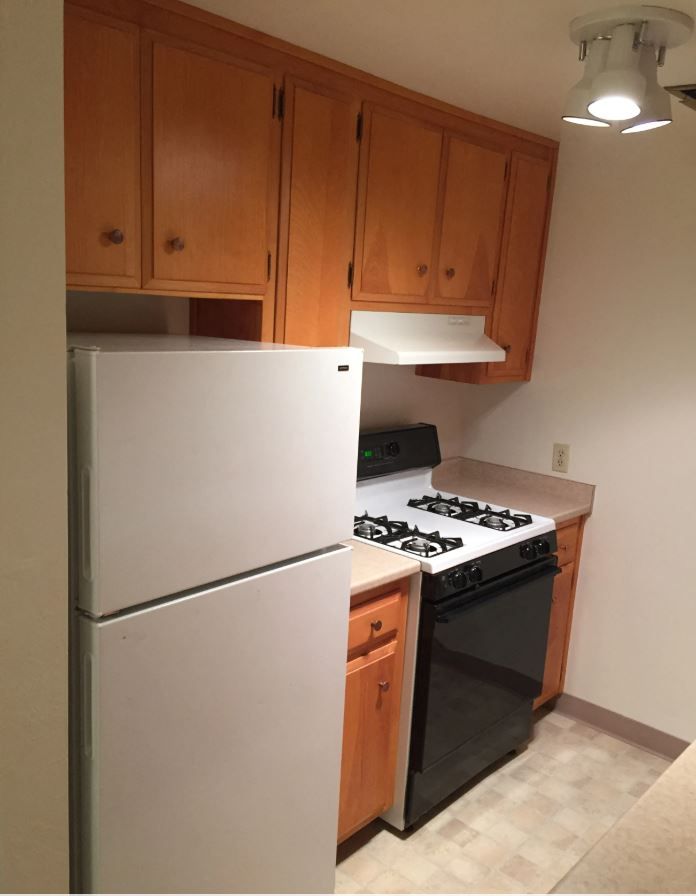 Small kitchen with white refrigerator, gas stove, and wooden cabinets.