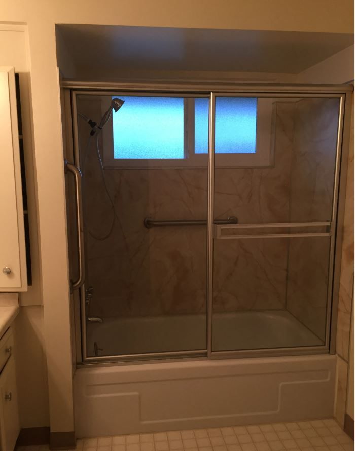A shower with glass sliding doors and a grab bar. Light beige walls and white tub surround.