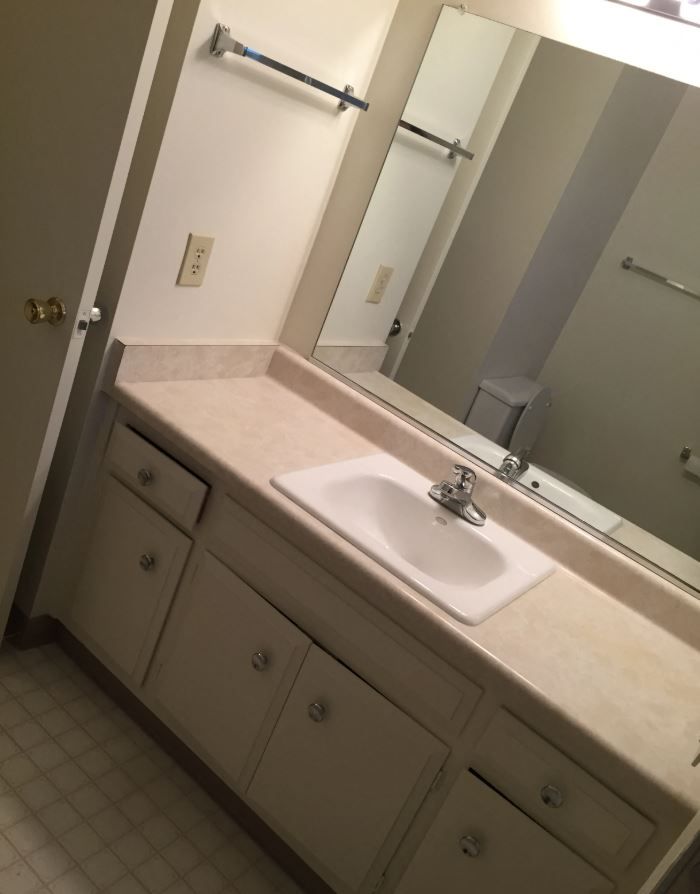 Bathroom with white vanity, sink, mirror, and tan countertop.