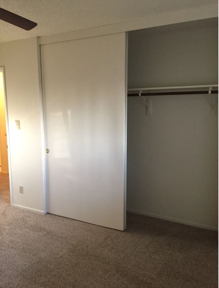 Ajar white sliding closet door in a room with beige carpet and an empty closet with a clothing rod.