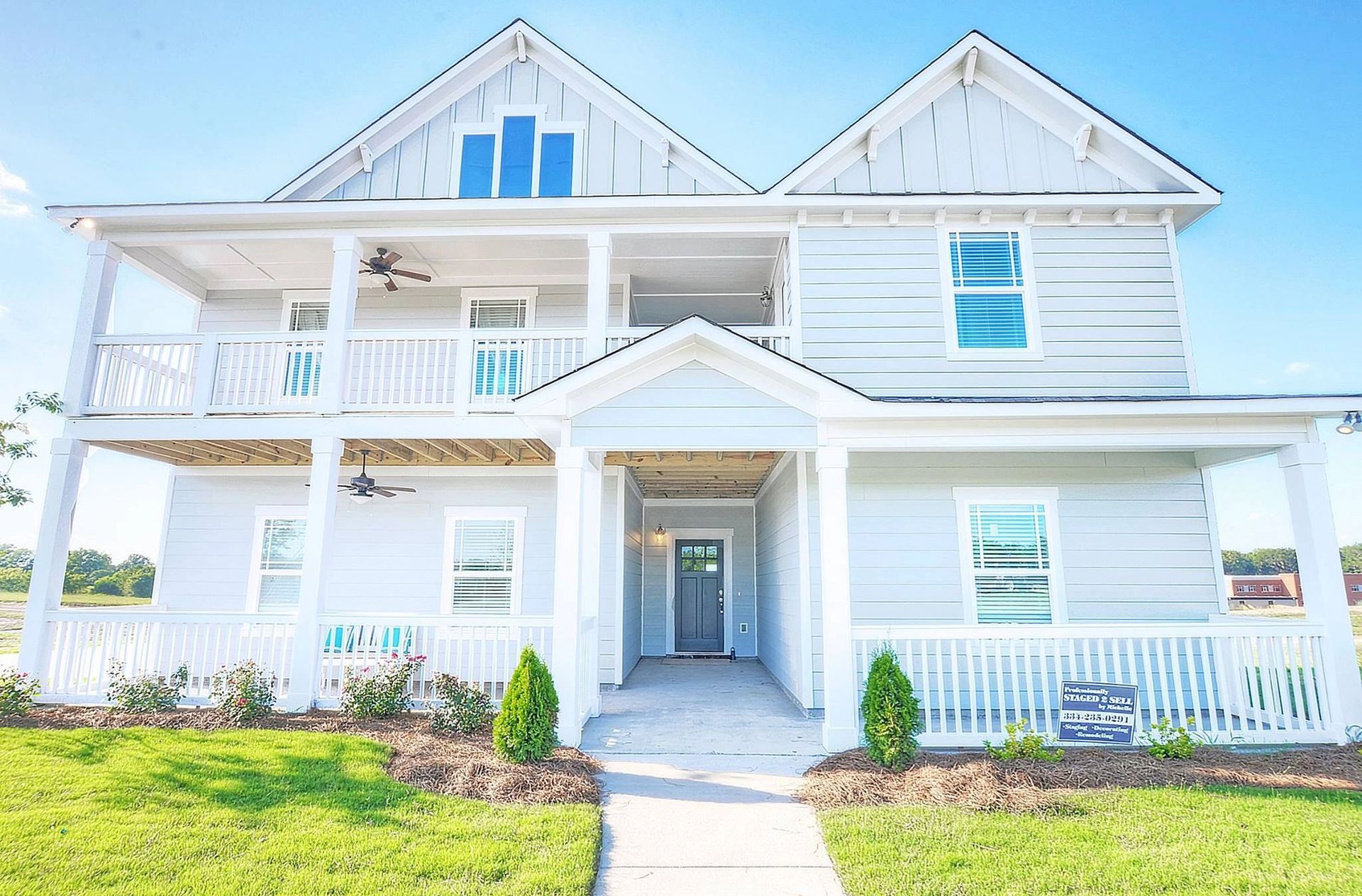 A large white house with a large porch and a blue sky in the background.