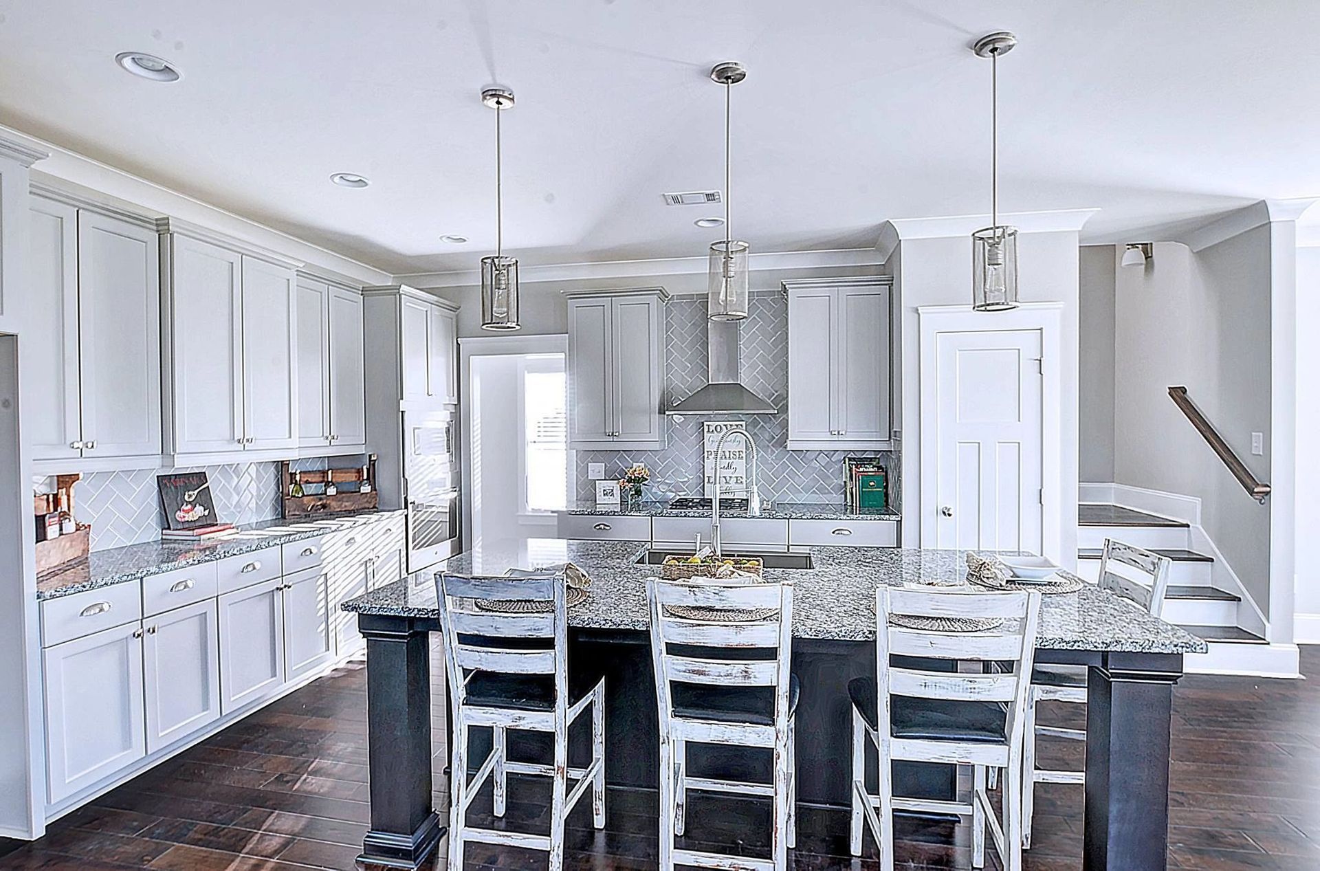 A kitchen with white cabinets , granite counter tops , stools and a large island.
